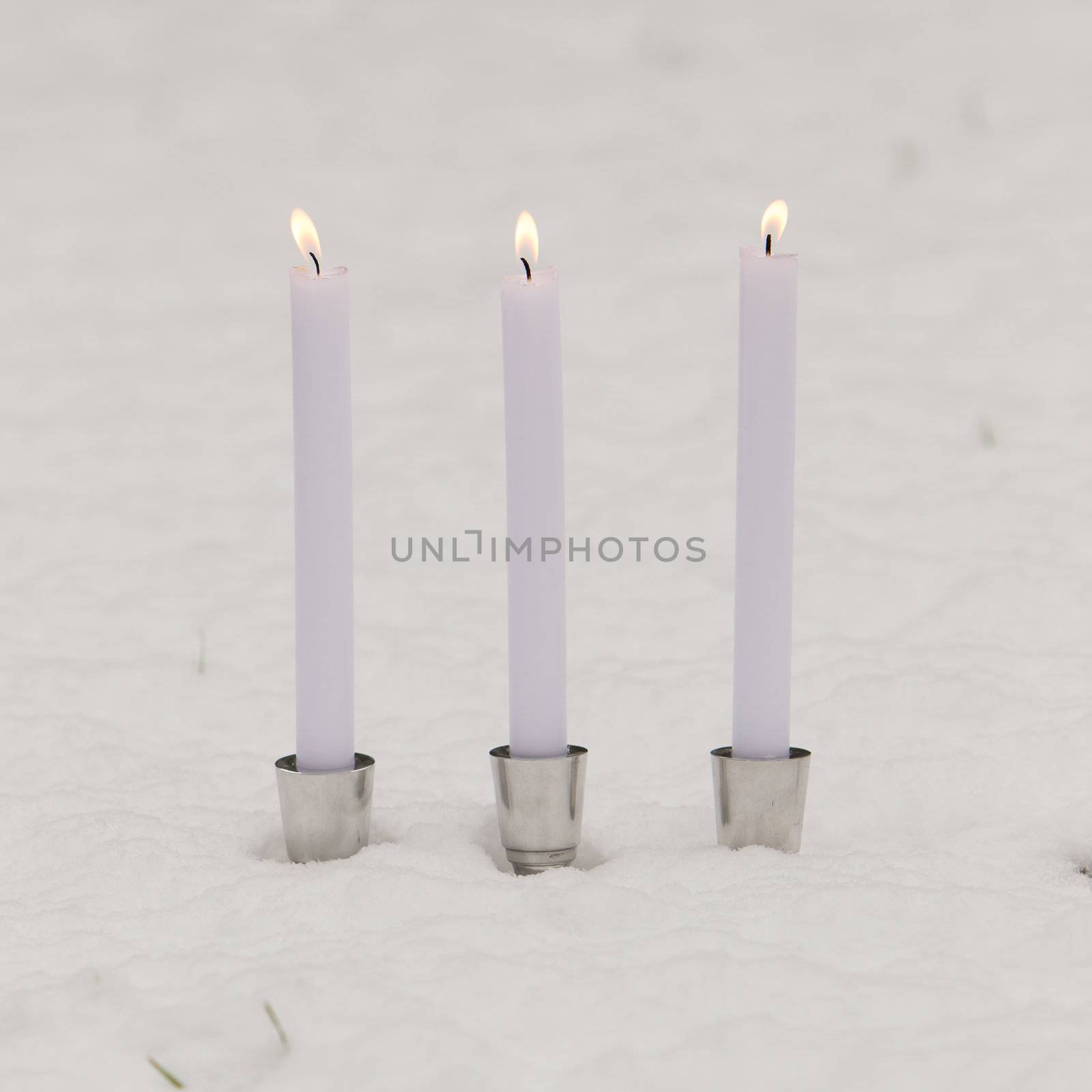 Three burning candles standing in the snow