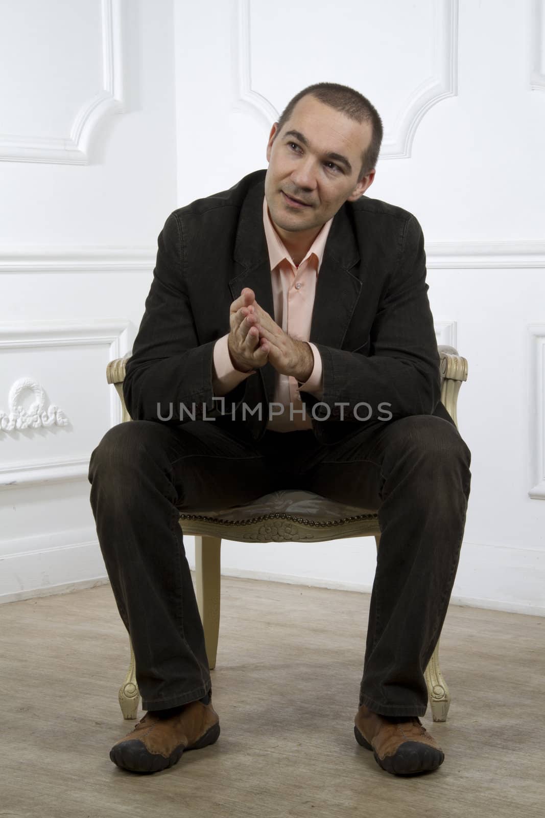 Man in a suit sitting on a chair and looks out of the frame with interest . Classic interior. Studio photography