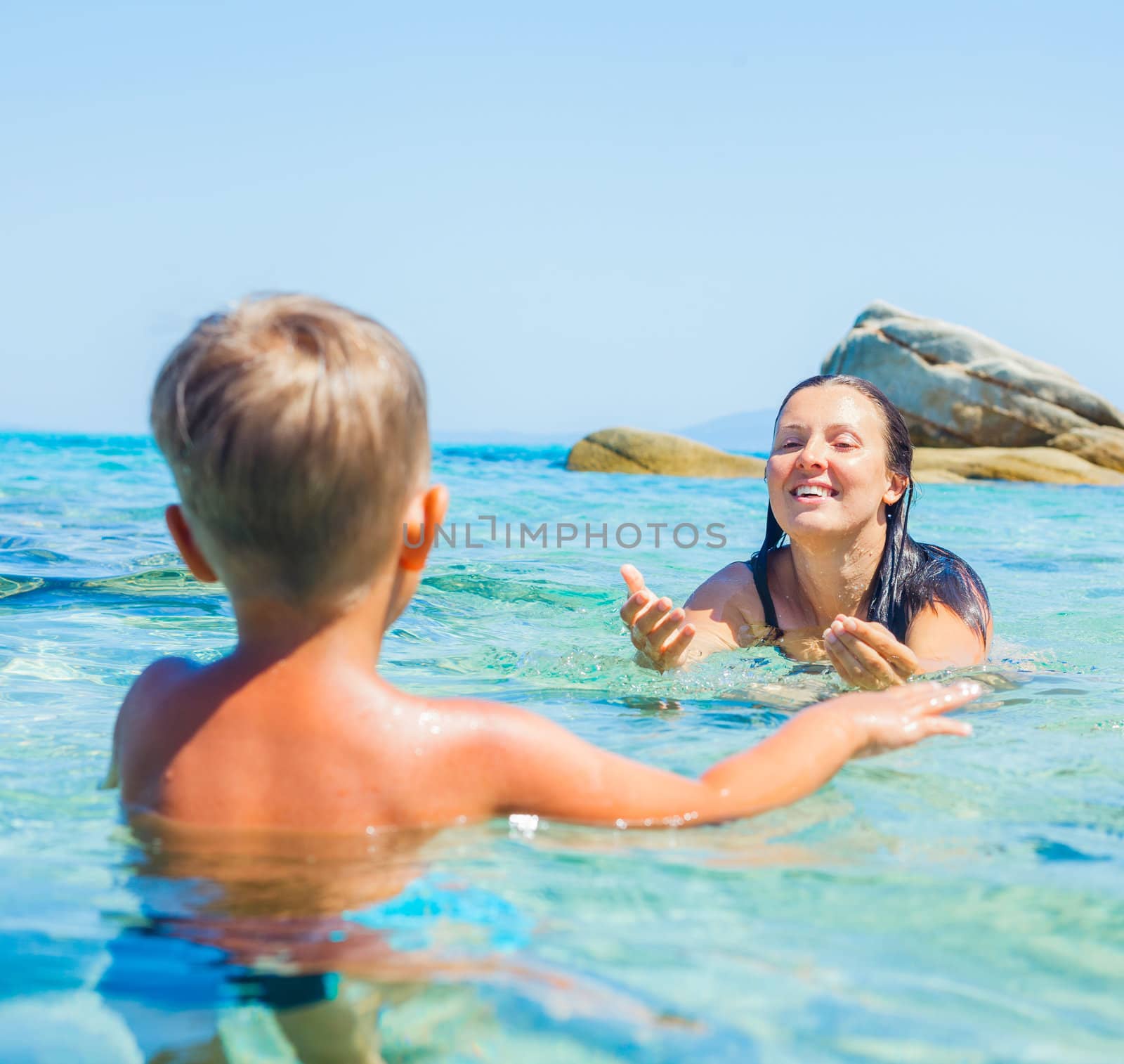 Happy young mother with her little son swimming in the transparent sea