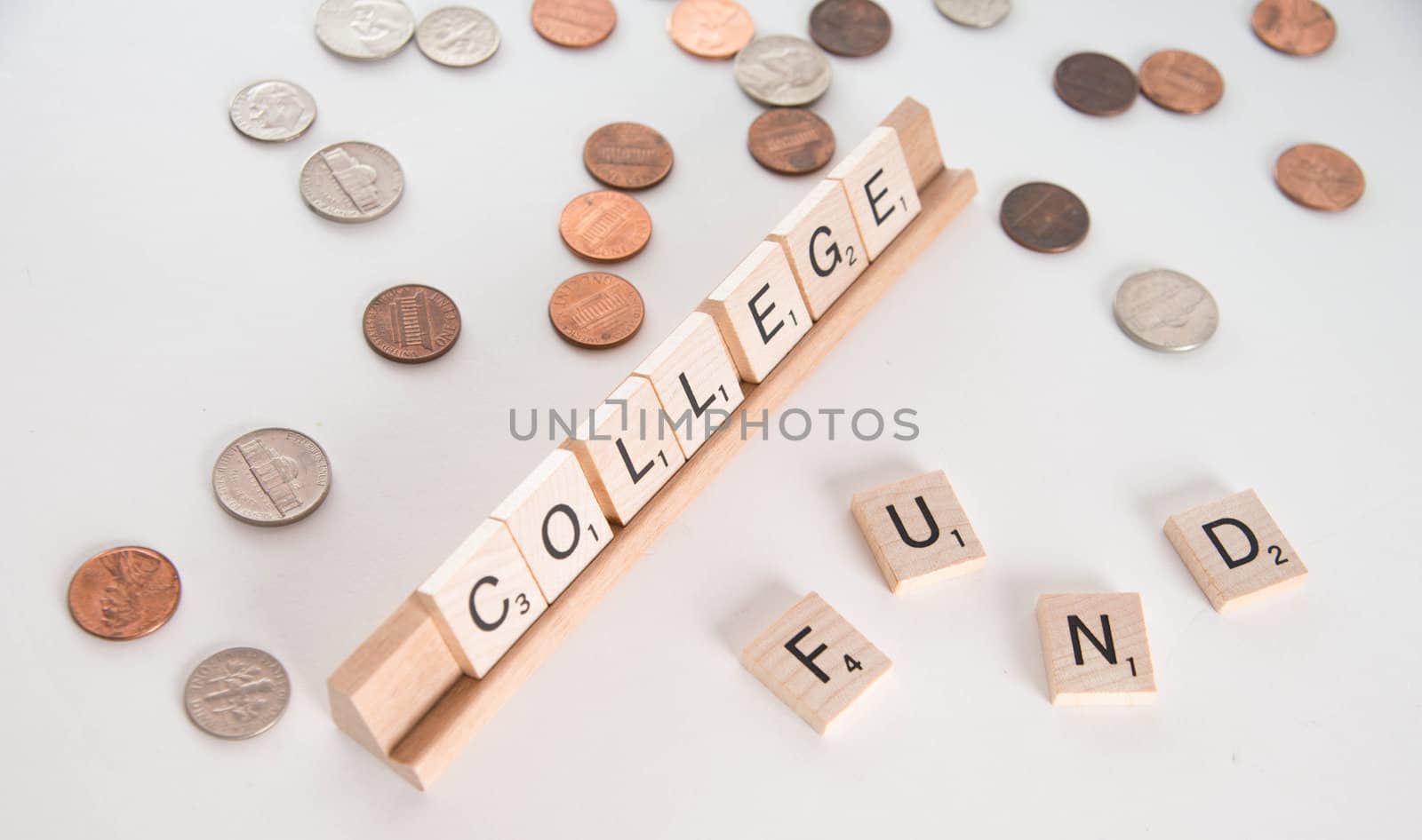 "College Fund" concept. Scrabble letters spell out "College Fund" with out of focus coins in background. Isolated on white background.