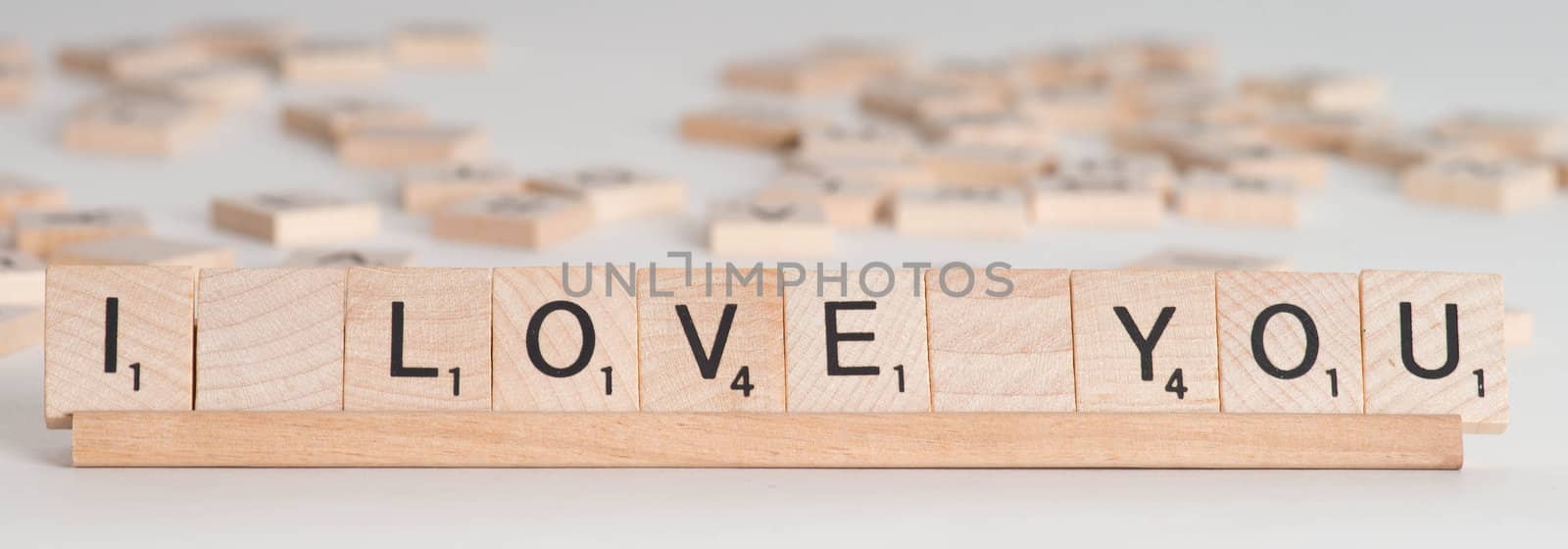 Wooden Scrabble letter spelling out phrase "I Love You".  Isolated on white background with light shadow.