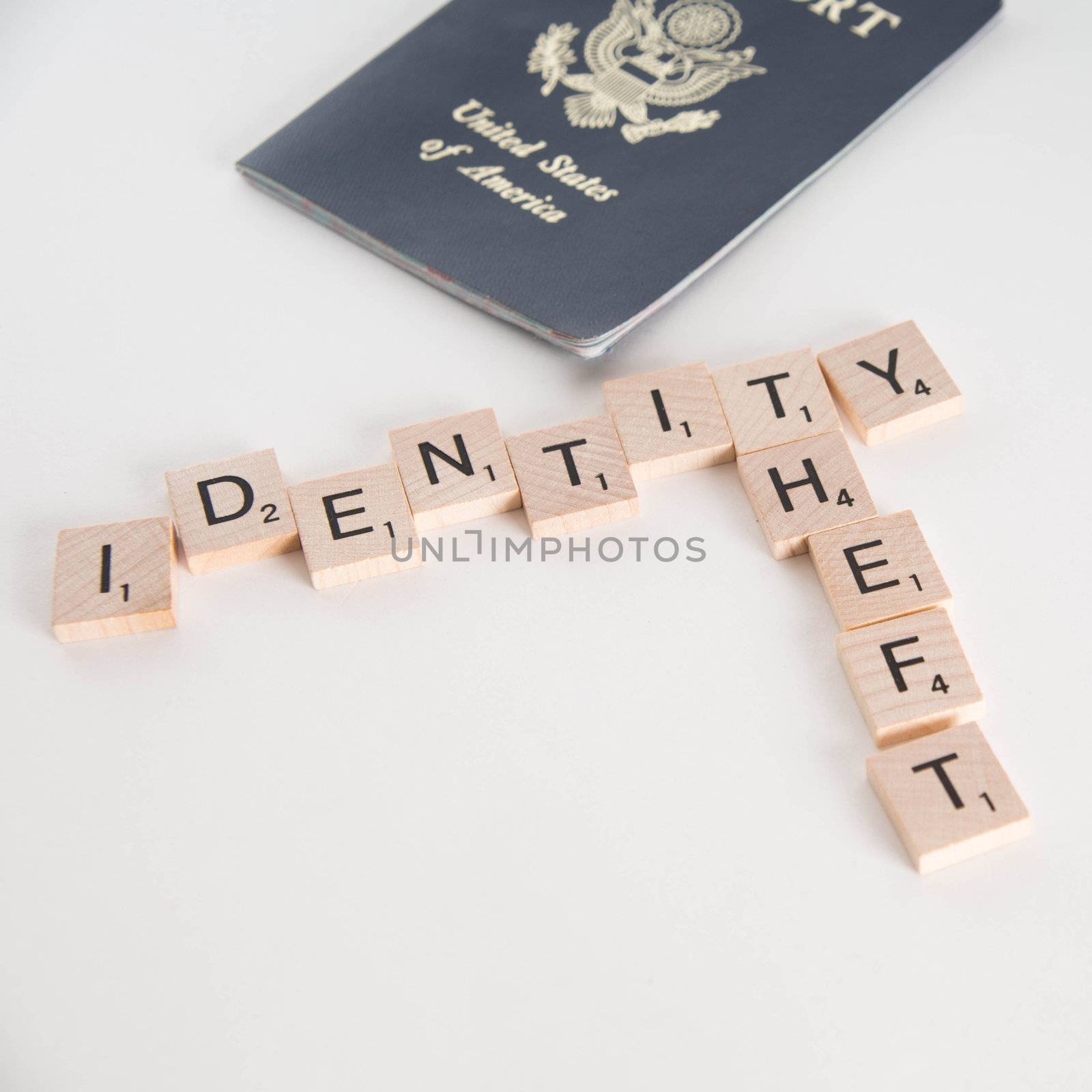 Identity theft spelled in Scrabble letters with US passport out of focus in the background. Isolated on white background.