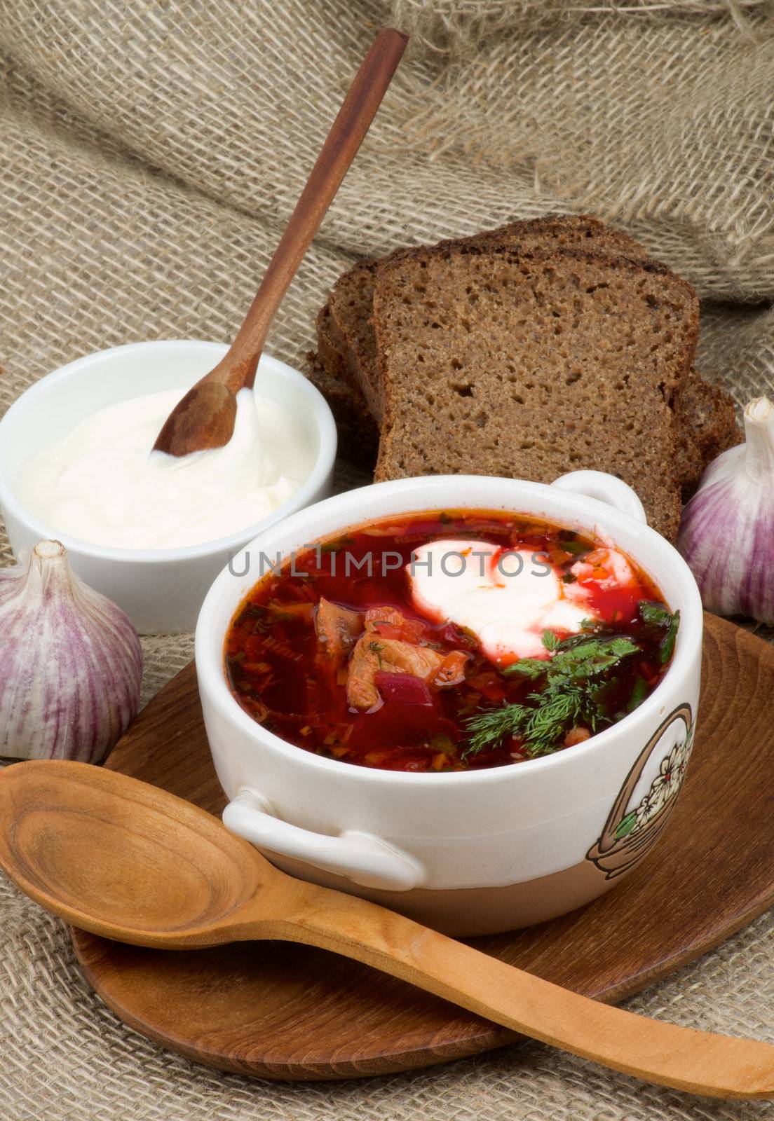 Arrangement of Traditional Soup with Beet, Vegetables, Meat and Brown Bread, Garlic and Sour Cream on Wooden Plate with Wooden Spoon