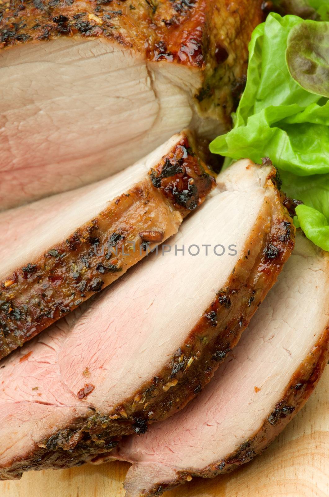 Slices of Ripe Roasted in Herbs Beef Medium Rare with Lettuce on Wood Cutting Board closeup