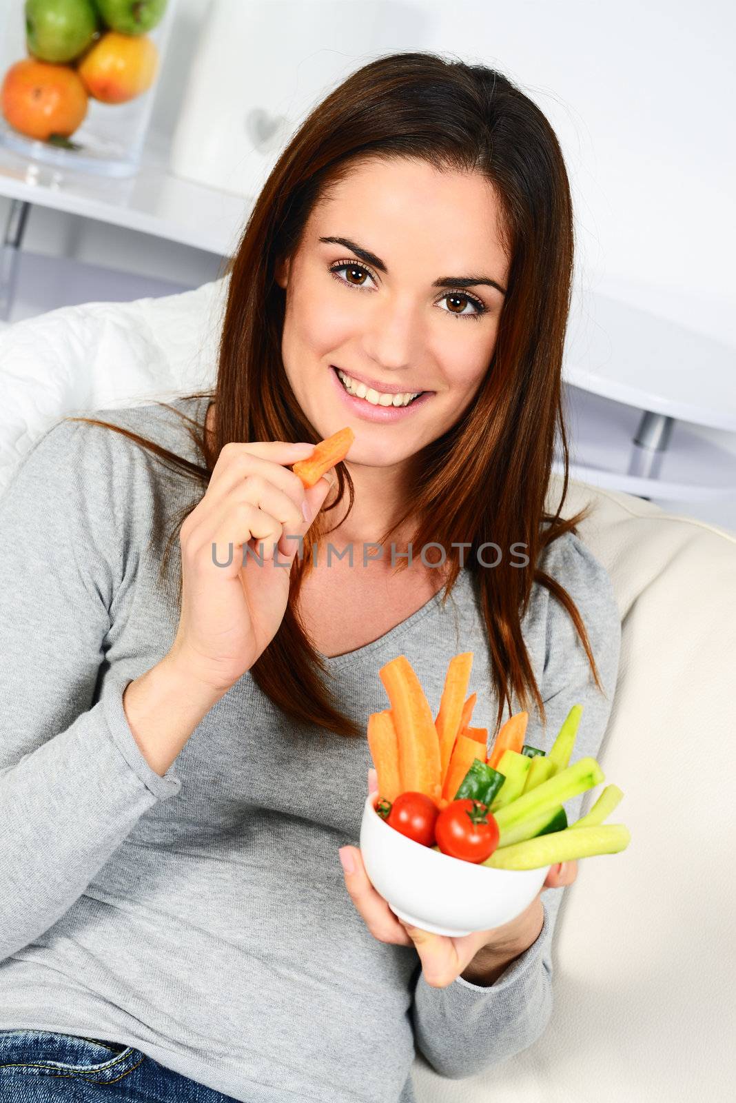Woman eating salad. Beautiful healthy smiling Caucasian woman enjoying a fresh healthy salad sitting in sofa looking up. High angle view with copy space on modern interior. 