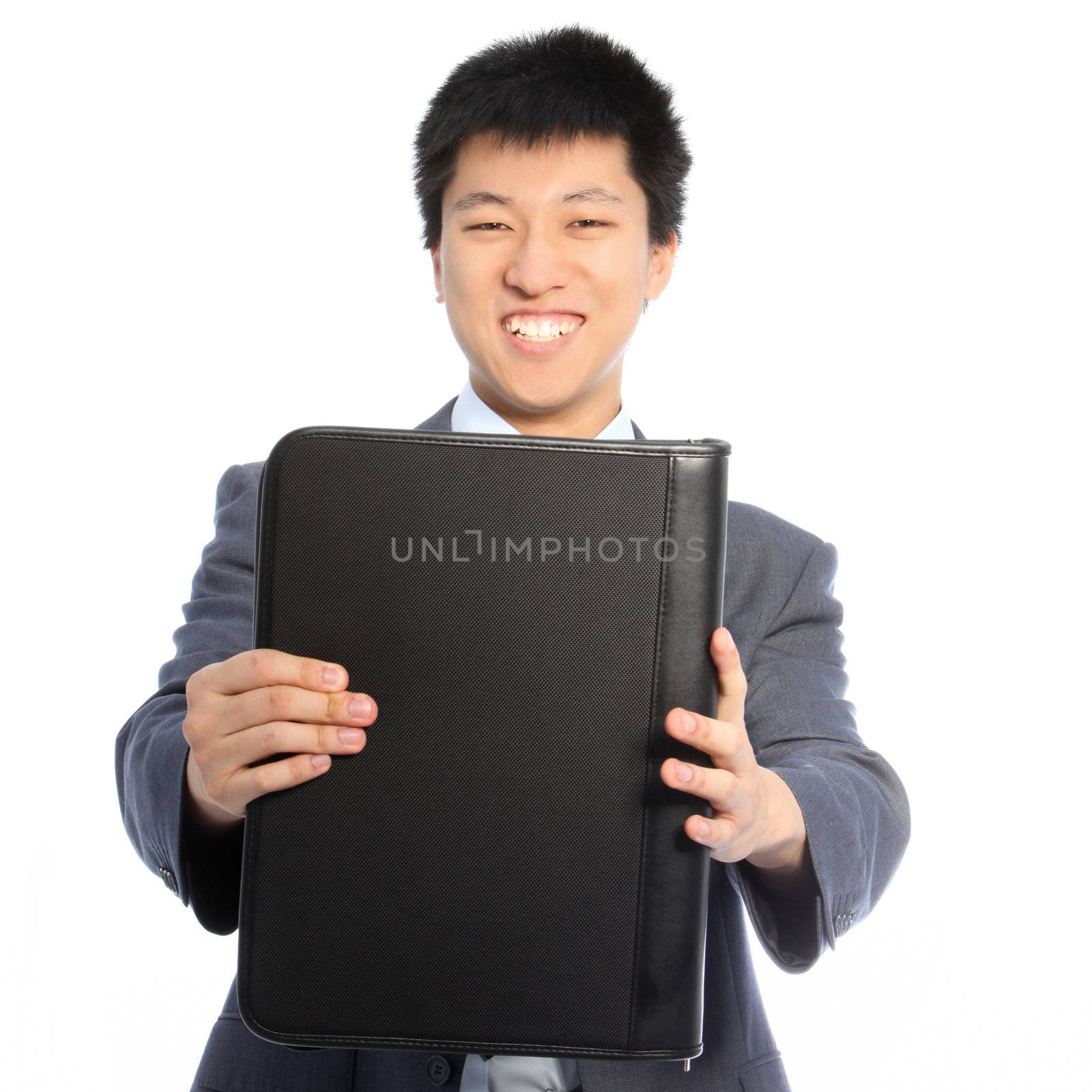 Smiling handsome young Asian businessman holding out a large black leather binder towards the camera isolated on white