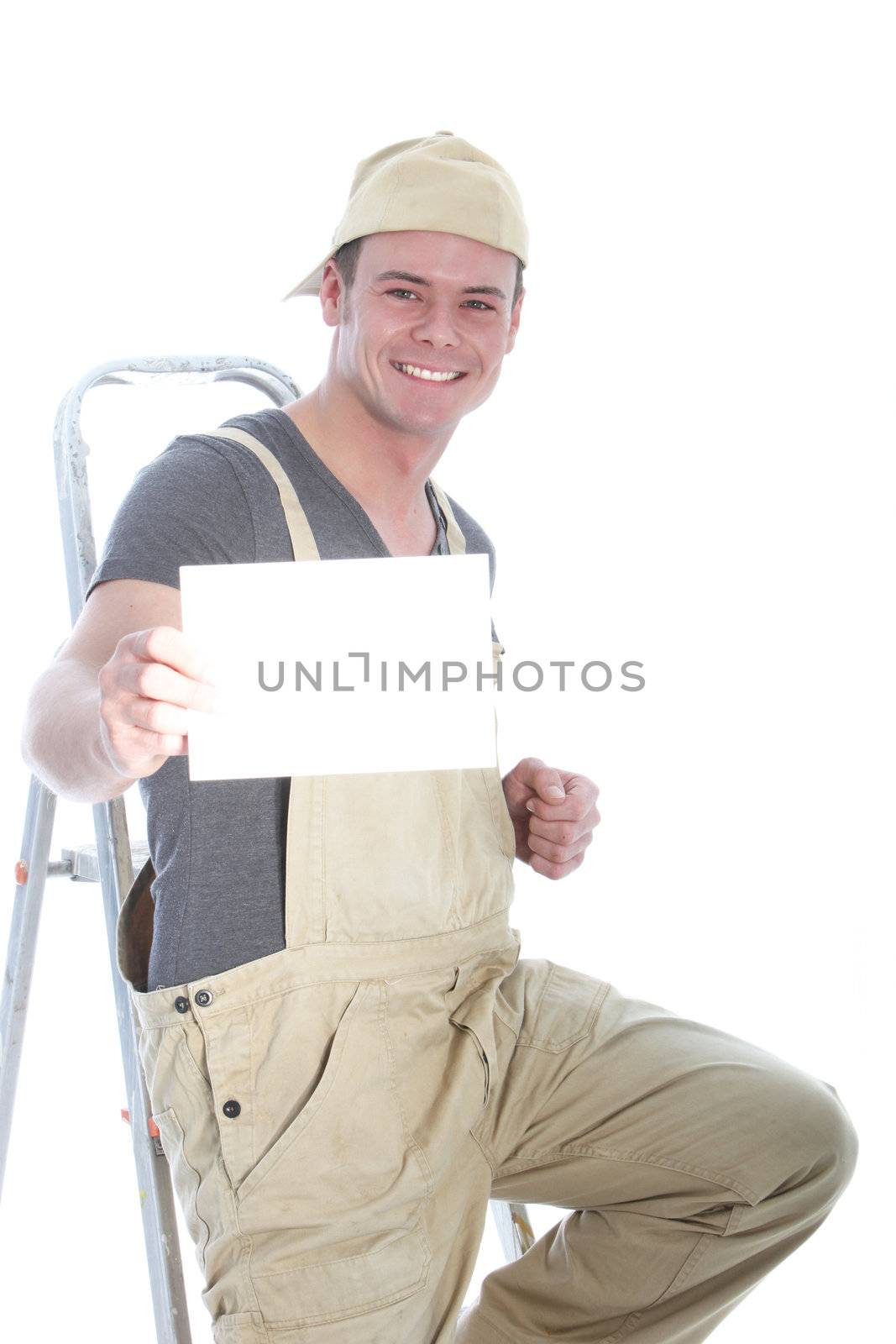 Confident young artisan in dungarees and a cap standing on his ladder holding up a blank sign with copyspace for your advert or text