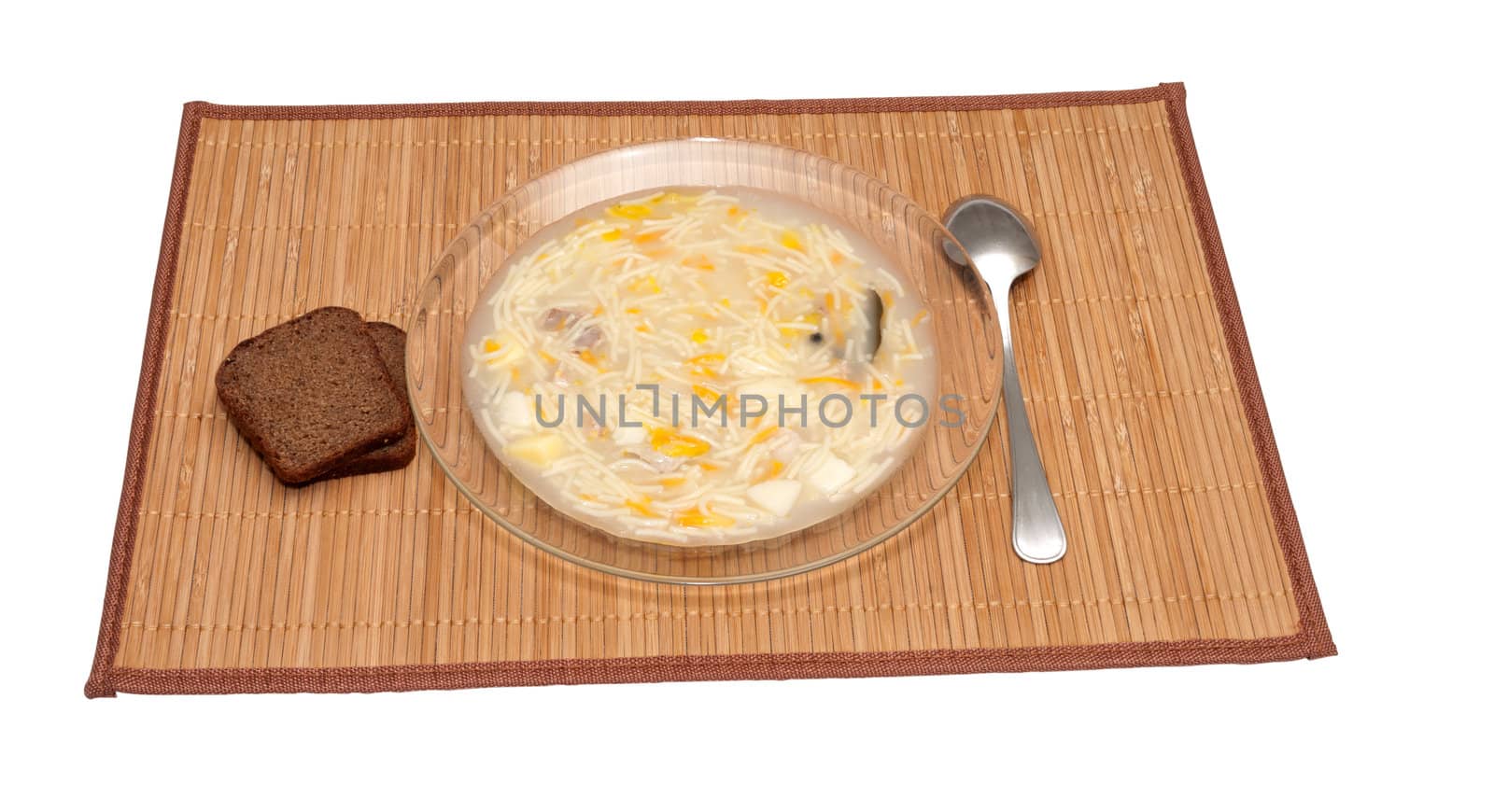 Plate of chicken soup and slices of rye bread on a bamboo napkin.