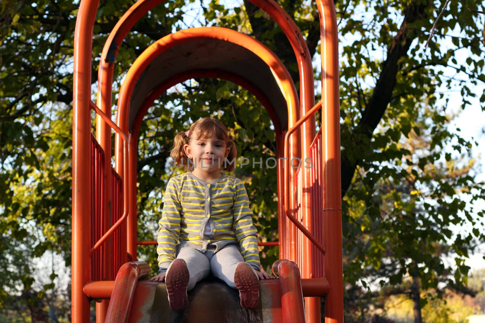 beautiful little girl sitting on playground slide