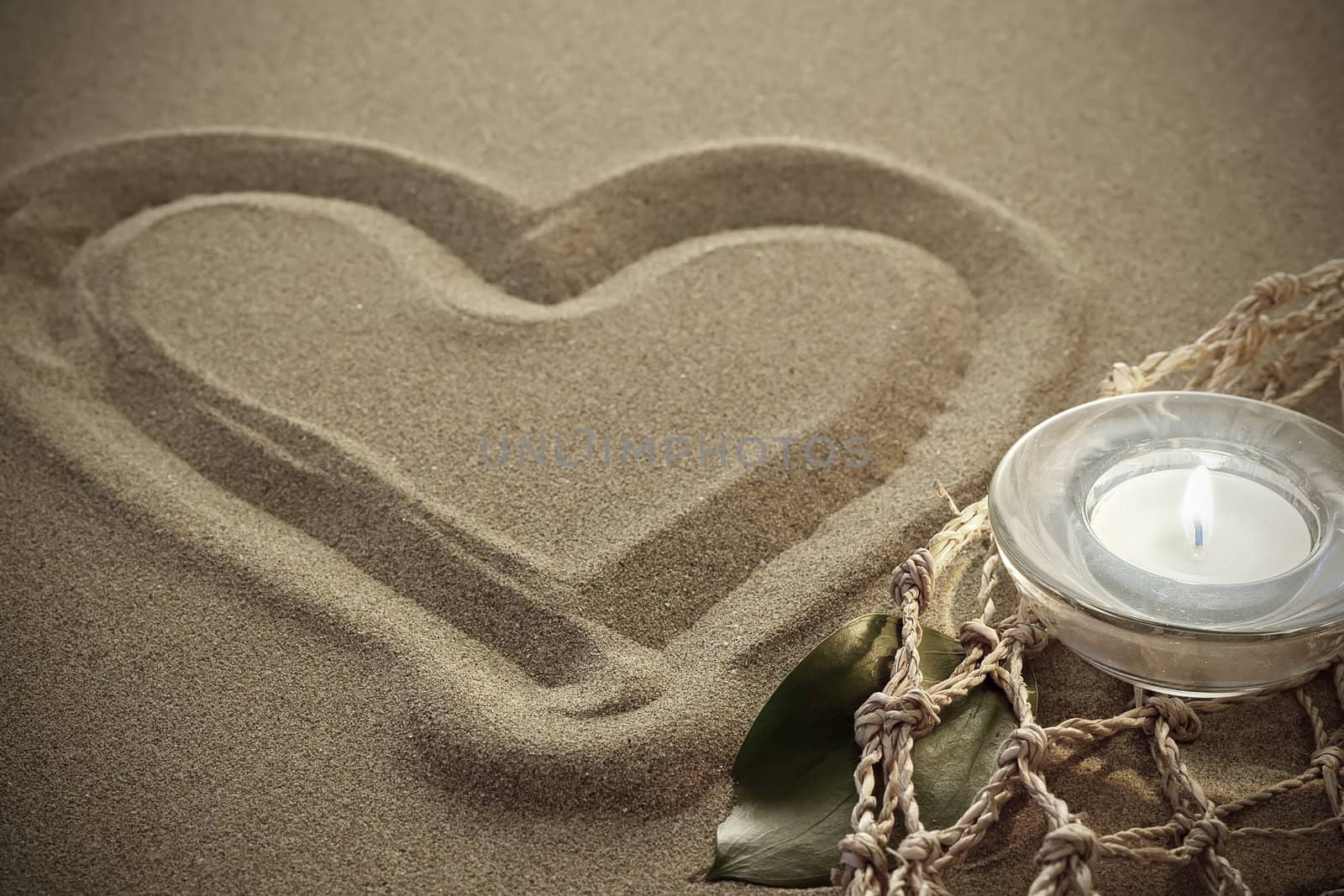 handwritten heart on yellow soft sand with lighted candles