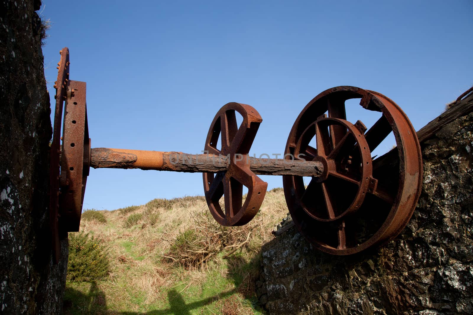 Vintage rusty industrial turning gear with a shaft supported by stone walls and wheels.