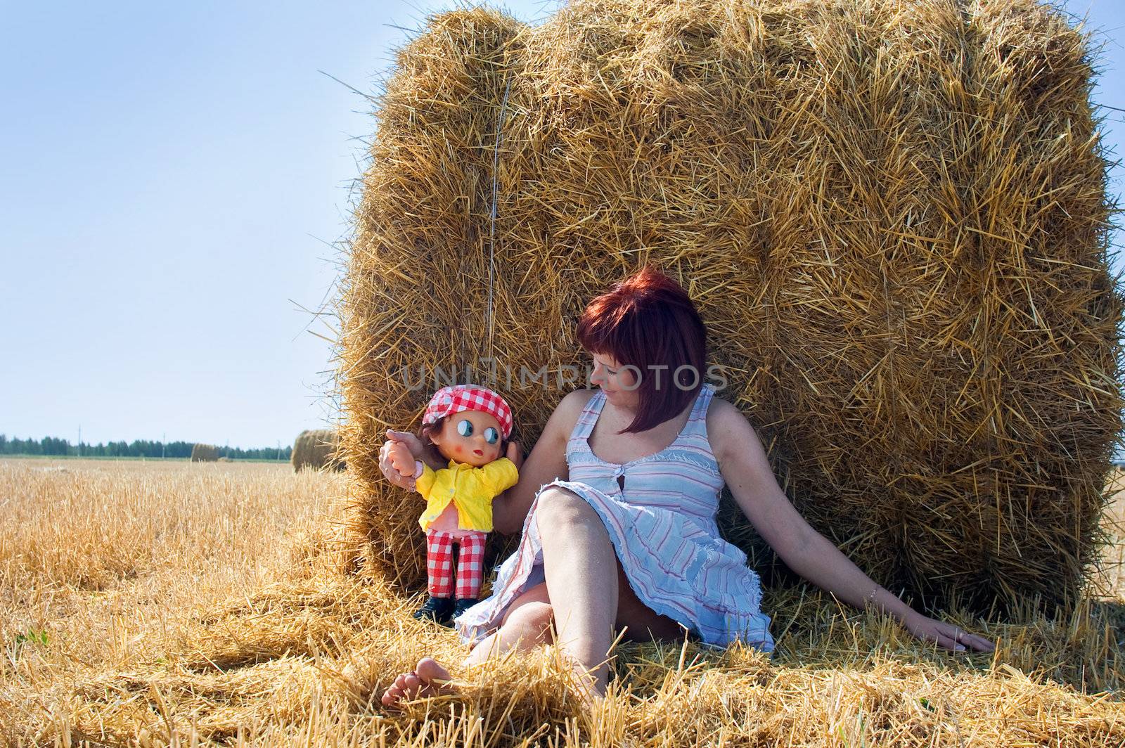 Woman with doll near the haystack in the field