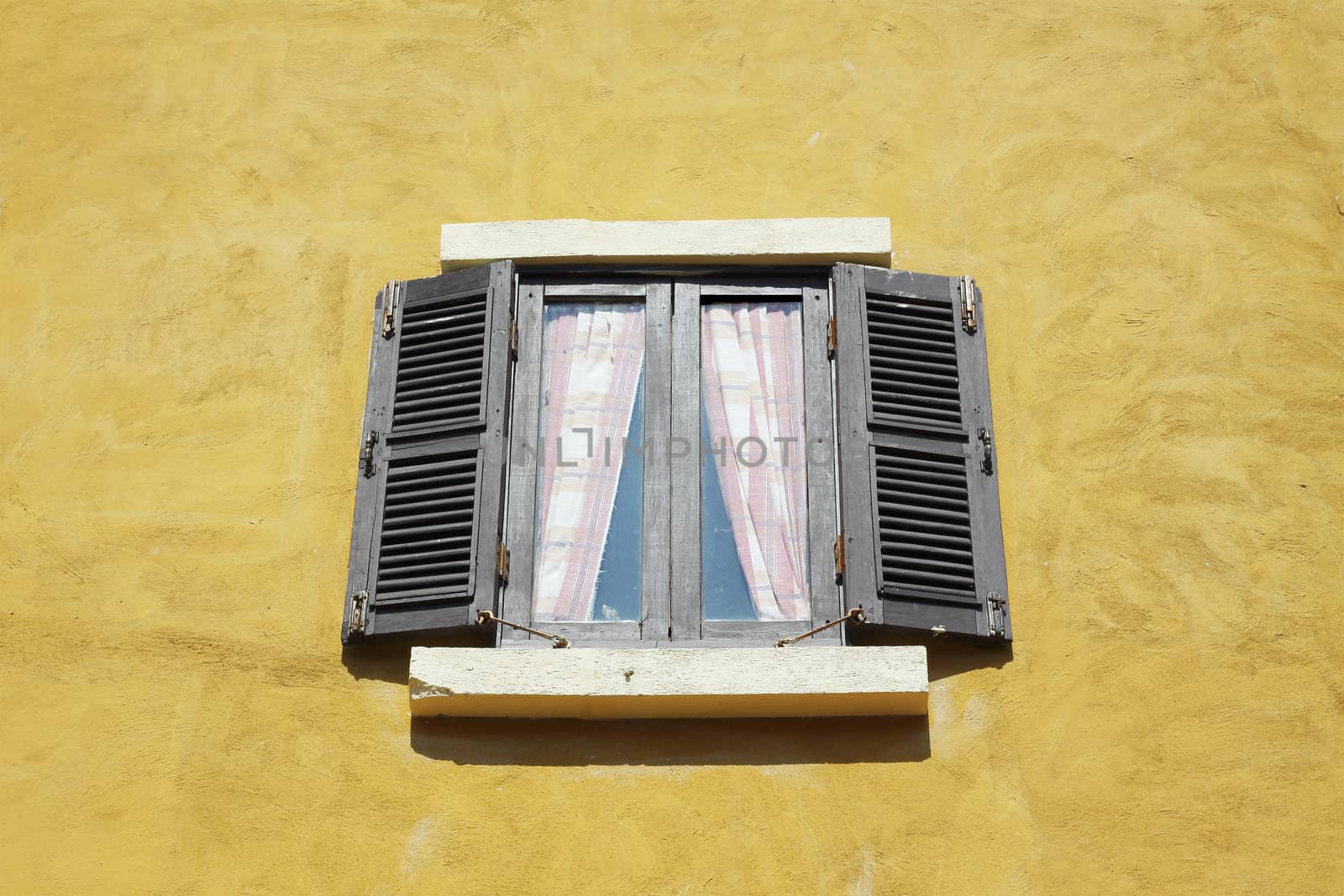 Old wooden window open on yellow wall.