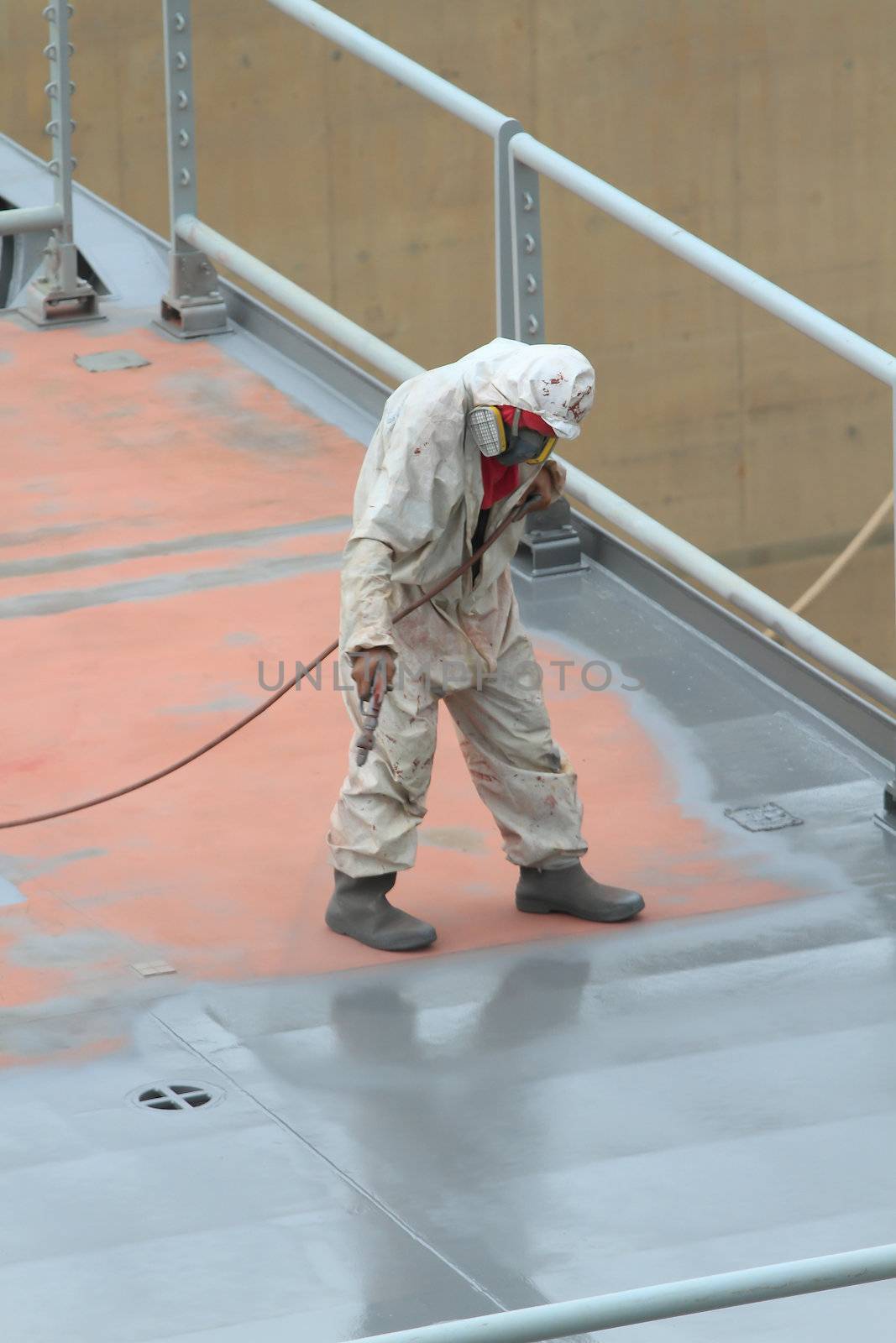 worker painting ship hull using airbrush gray paint