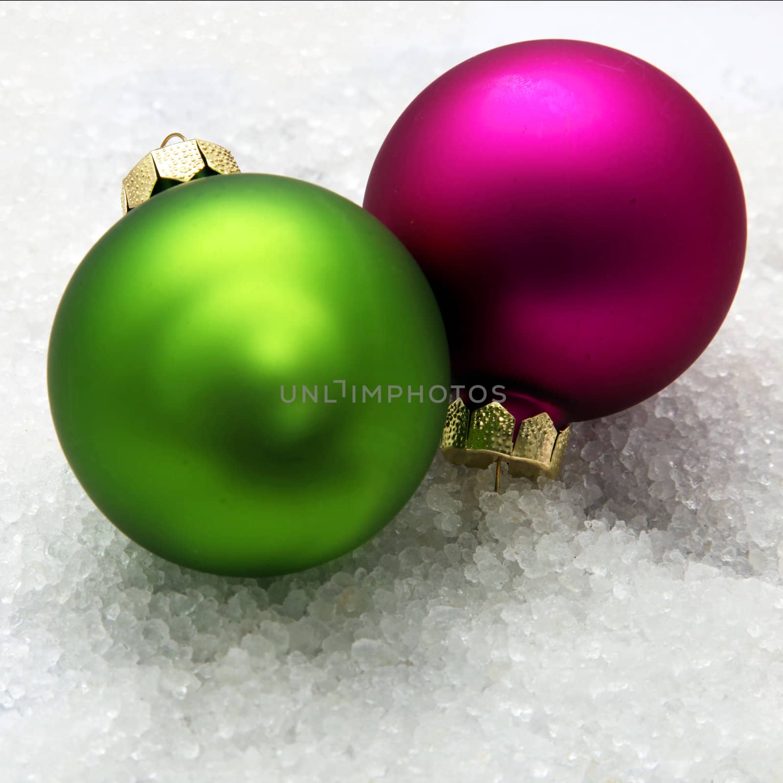 Two Christmas globes, green and violet in the snow, close up