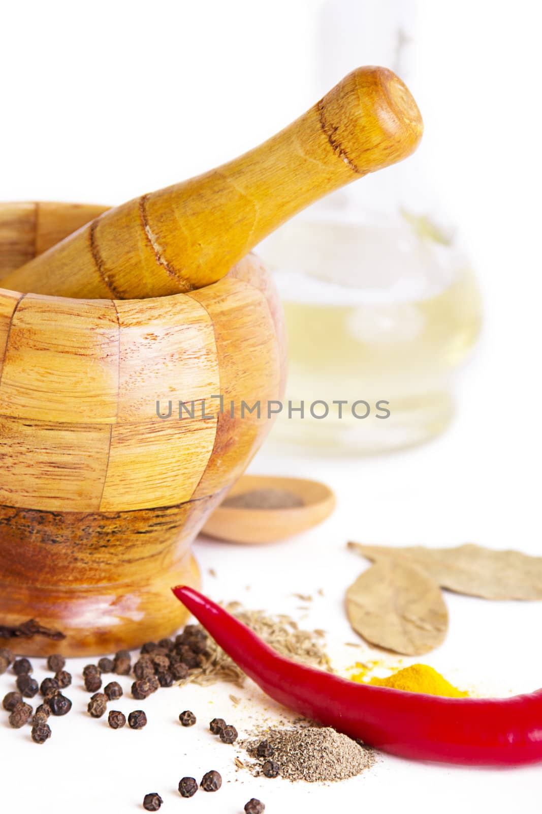 Mortar with pestle, variety of spices and oil over white
