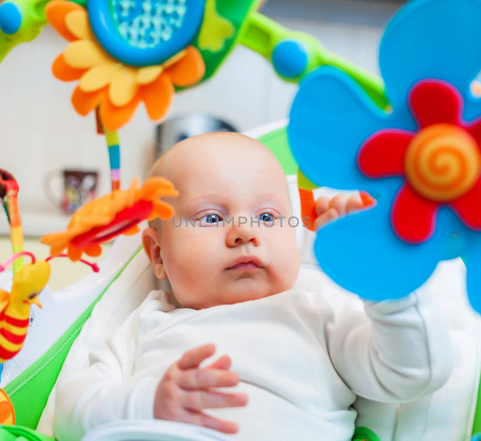 Closeup portrait of sweetest baby girl playing with a colorful mobile toy