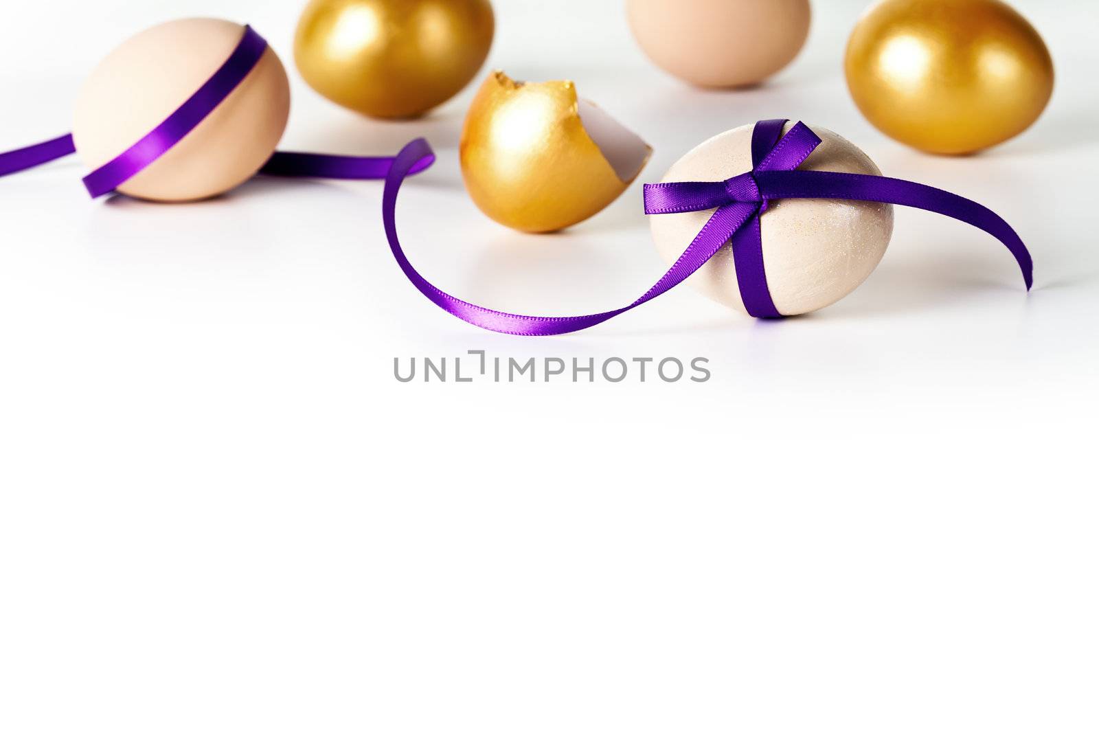 Easter egg with violet bow on white background. Composition with beige and gold eggs