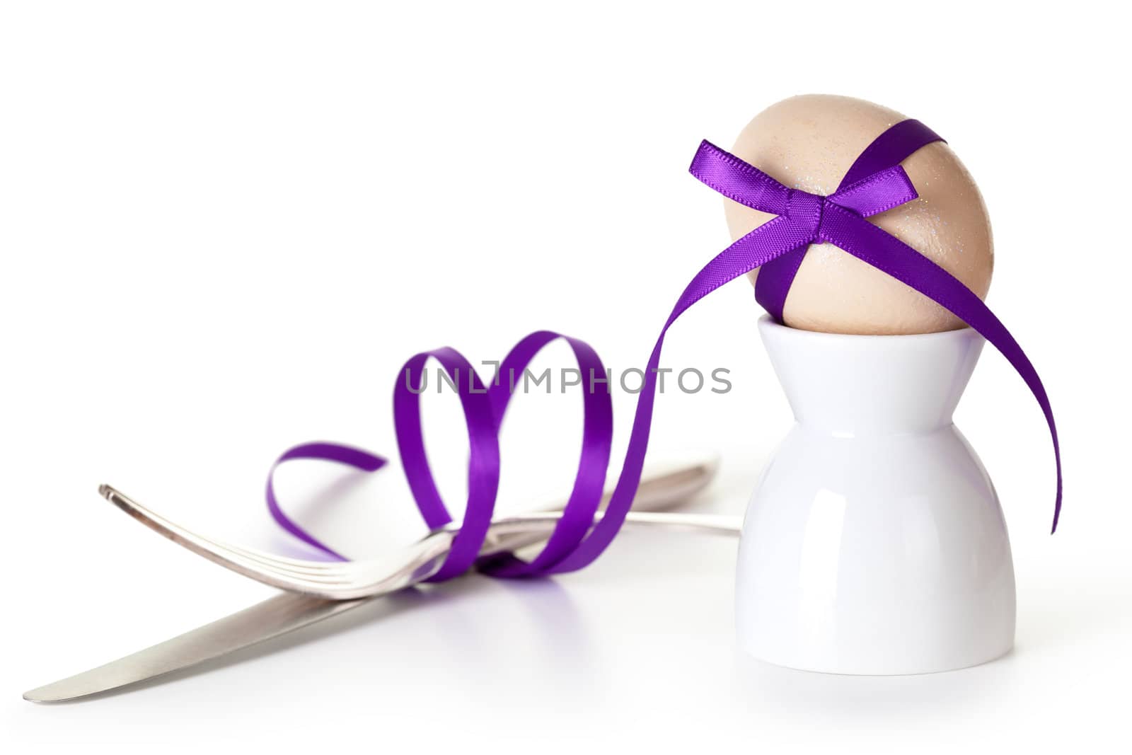 Easter egg with violet ribbon on white background. Composition with cutlery and egg hand painted a beige paint with glitter