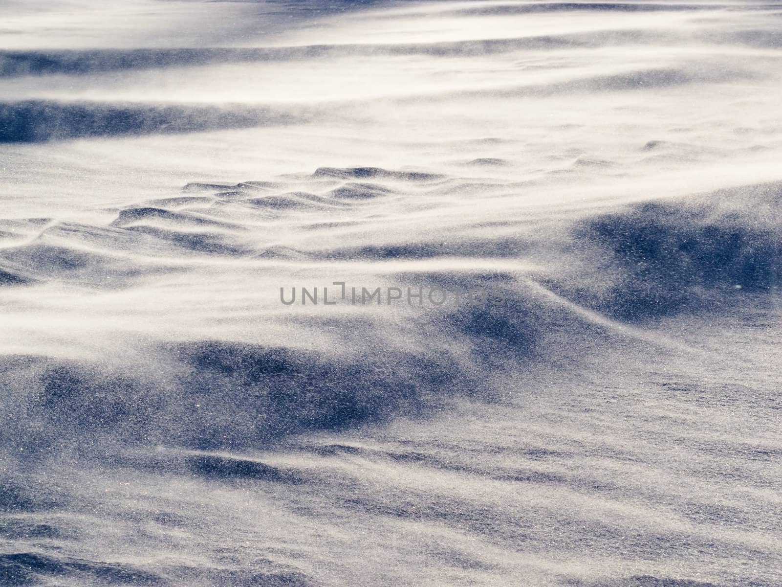 Blizzard background texture pattern: drifting snow crystals driven by strong wind creating snow surface refief