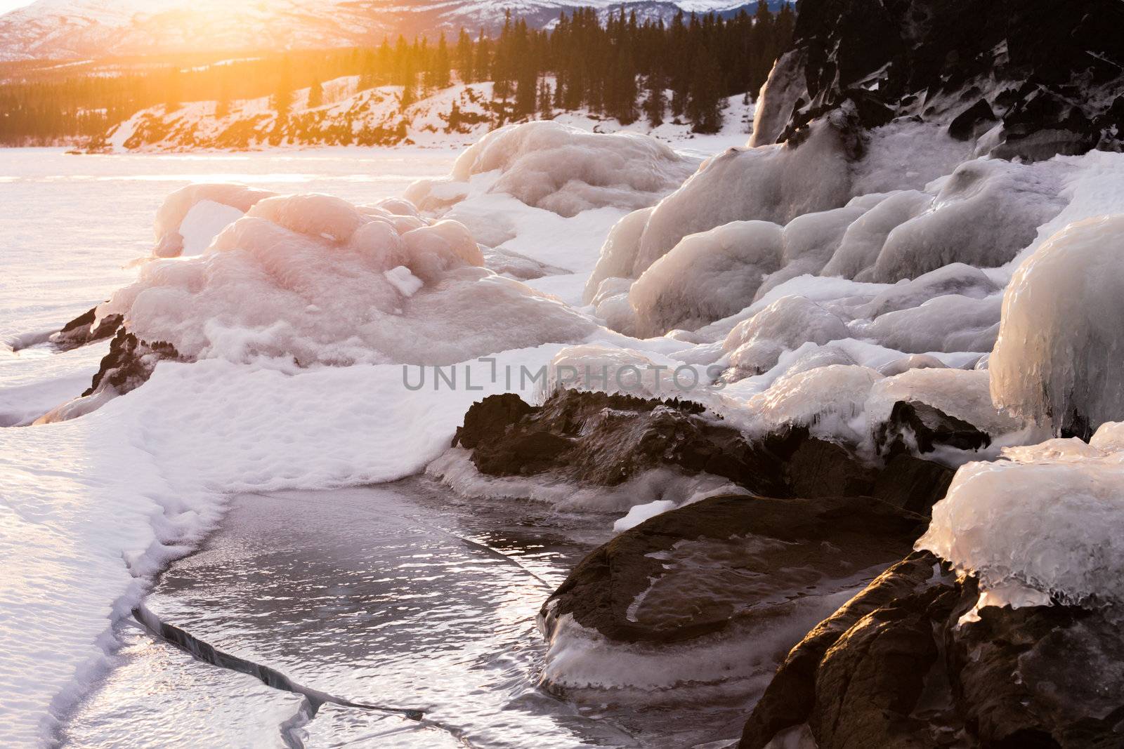 Warm energy of glowing orange sunlight over snow and ice-encrusted rocks of a beautiful northern winter landscape.