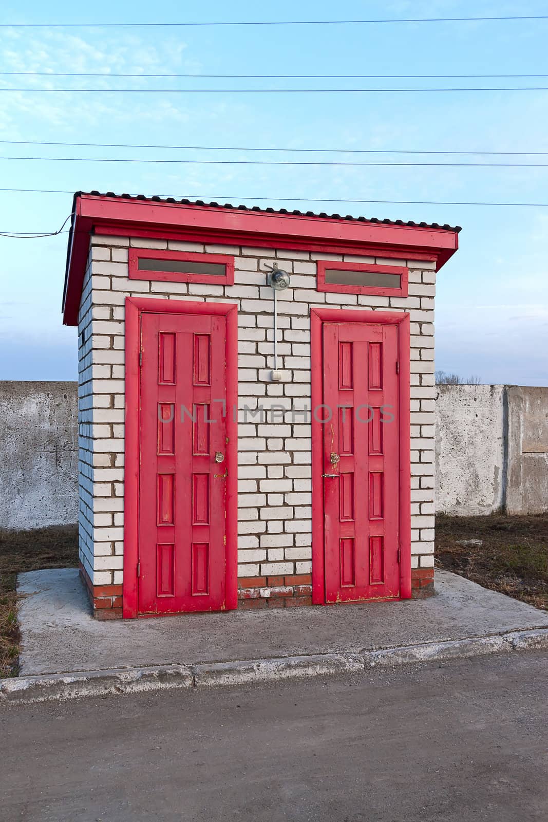 Toilet building with red doors on  wall against  blue sky.