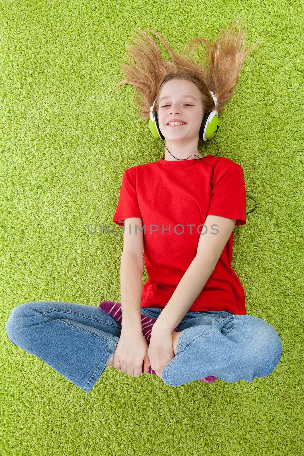 girl is listening to music with headphones on lying in green carpet