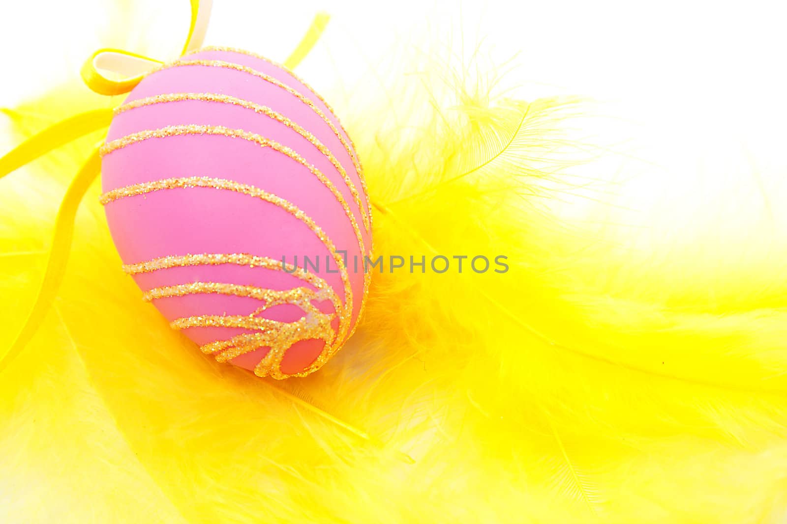 Pink easter egg on yellow feathers in closeup