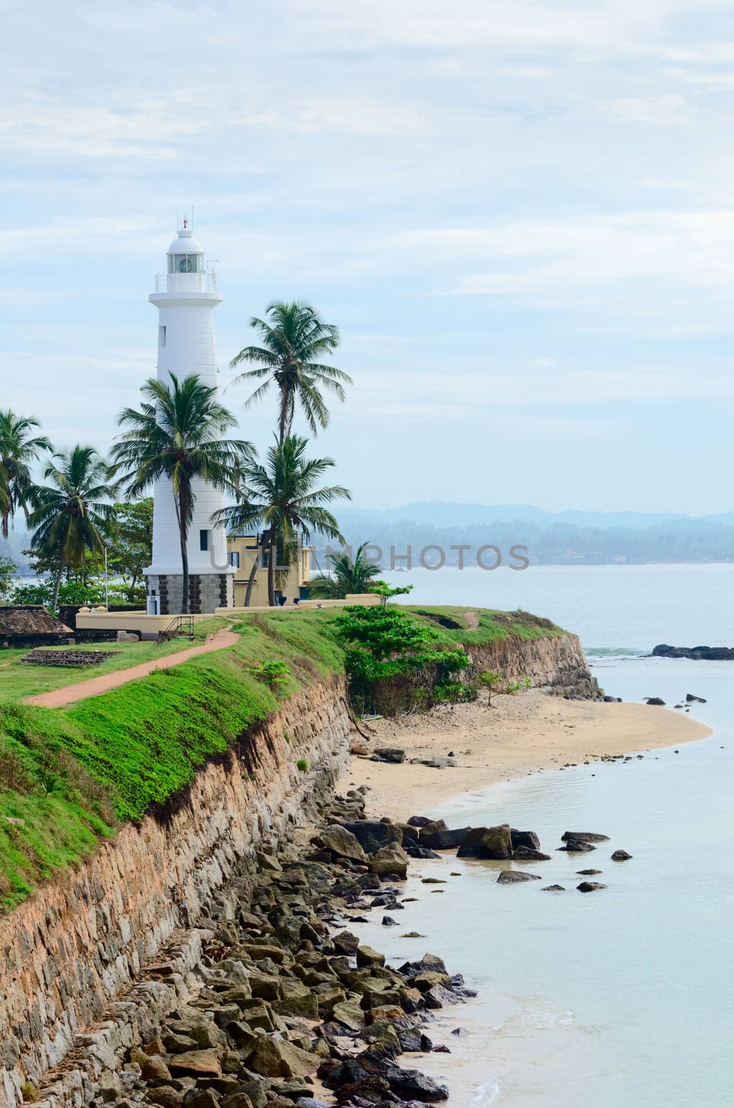 White lighthouse on fortified stone wall with cloudy sky background, Galle, Sri Lanka
