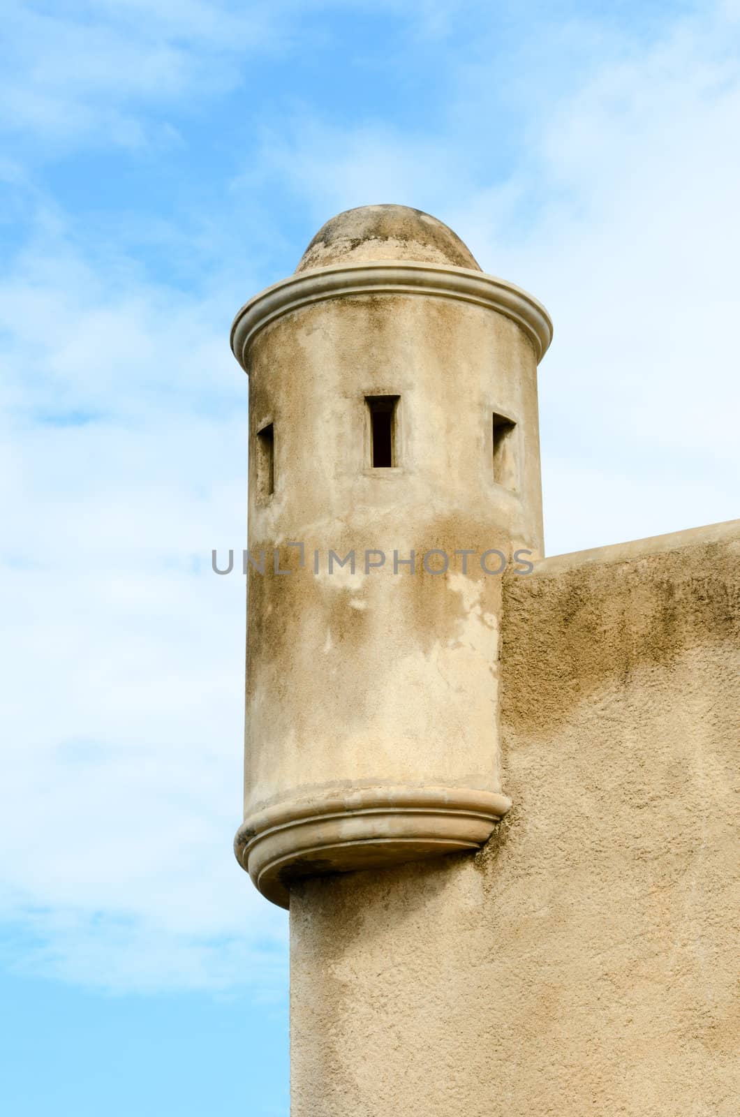 One light military tower with gun slots above fort wall with cloudy background