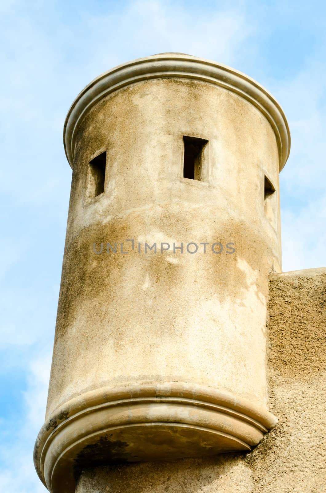 Old military tower with gun slots above fort wall with cloudy background
