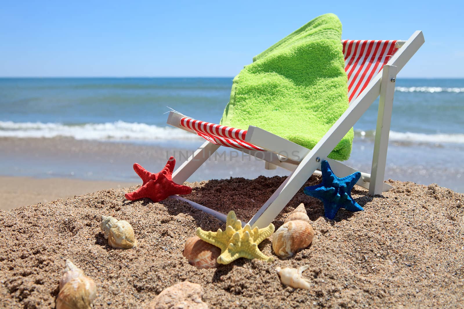 Beach chair and green towel near the ocean with shells on sunny day