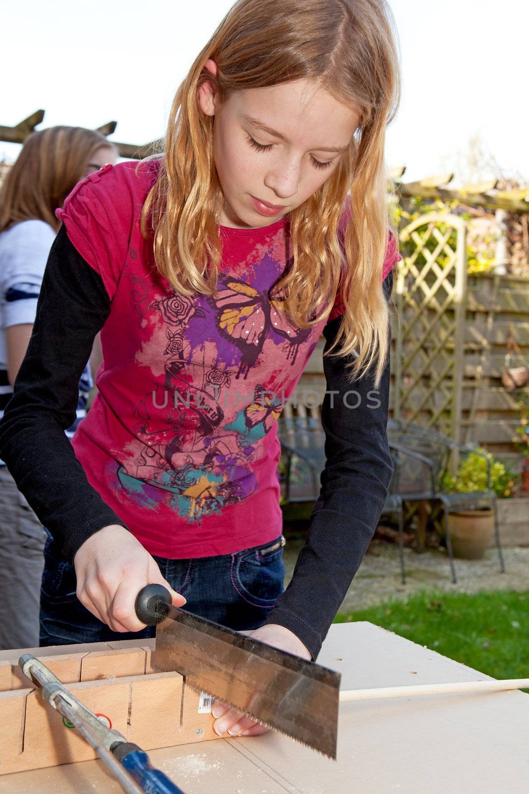 Young girl is sawing a wooden stick