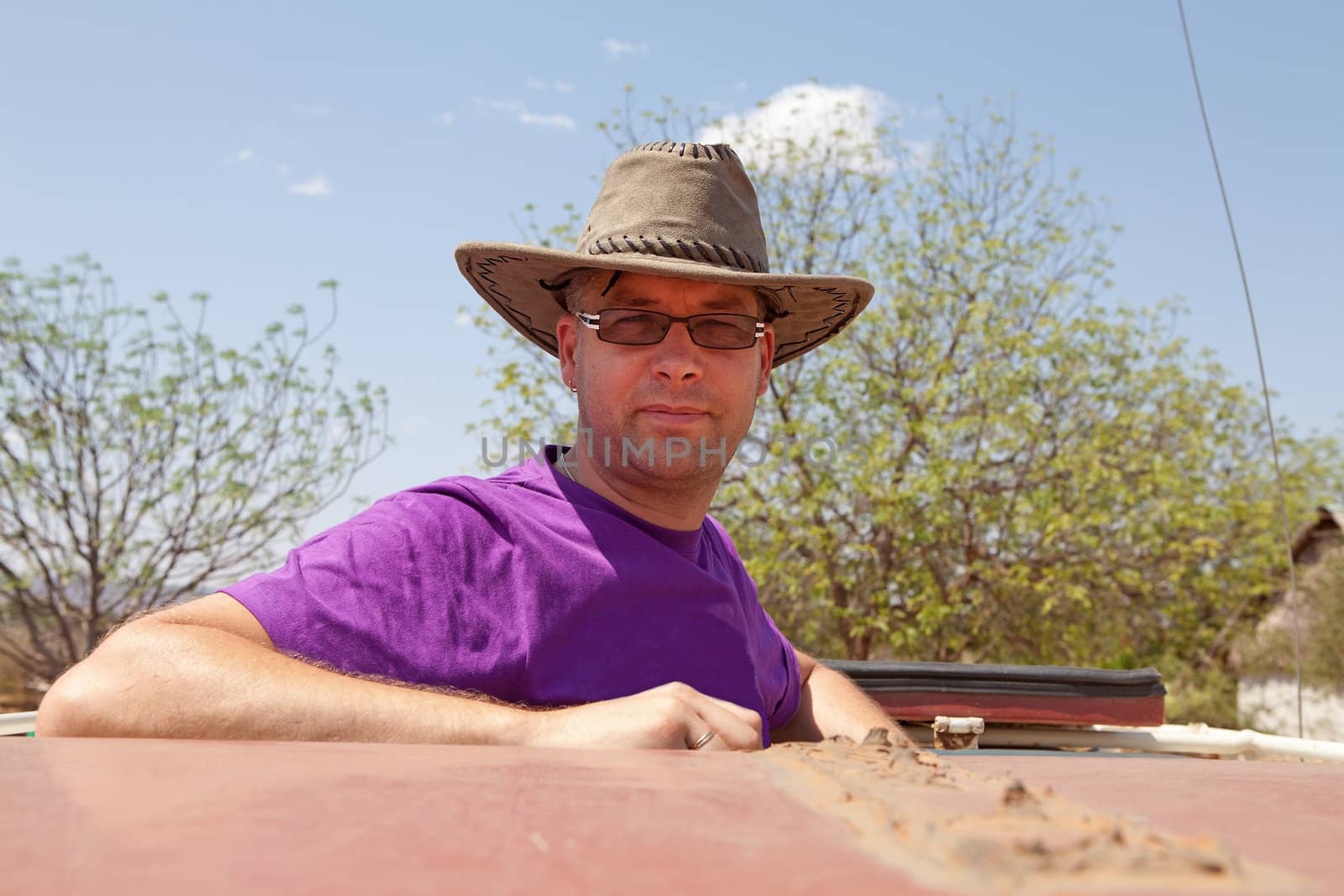 Going on safari: man standing on top of jeep with hat on