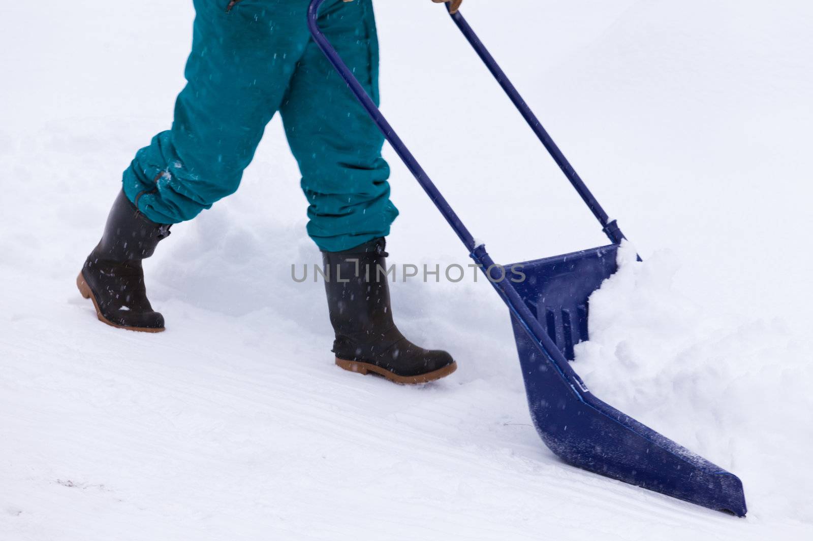 Manual snow removal from driveway using a snow scoop by person wearing boots
