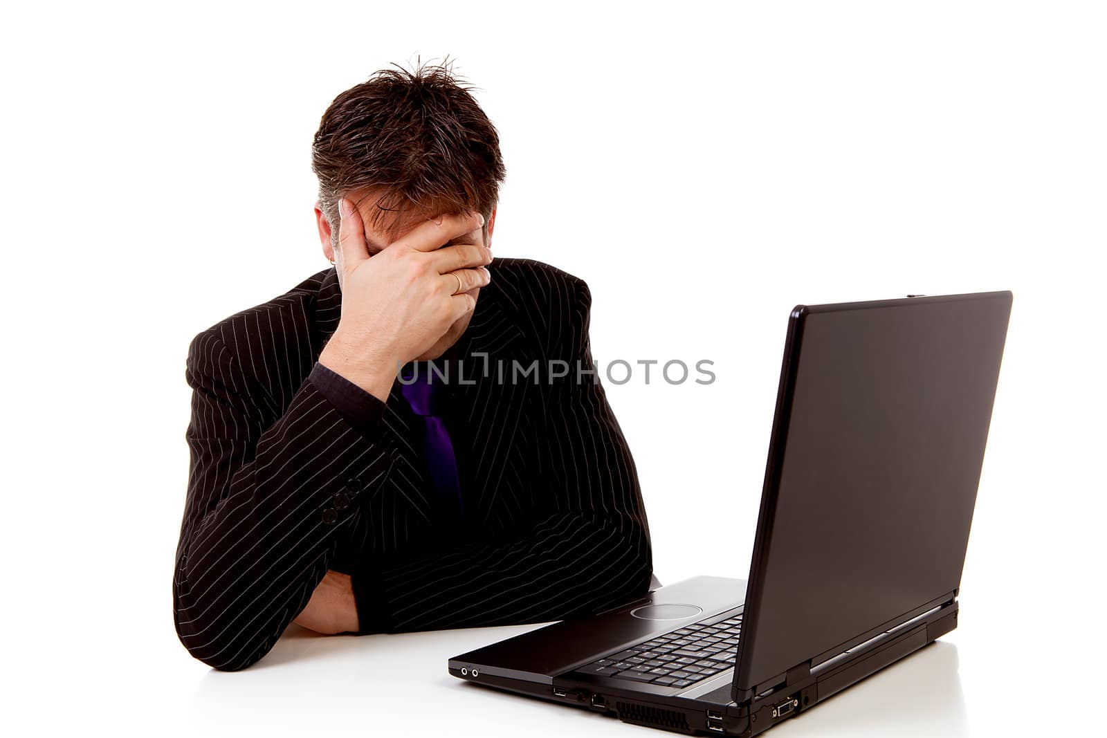 Businessman sitting behind desk is in despair, covering his eyes, over white background