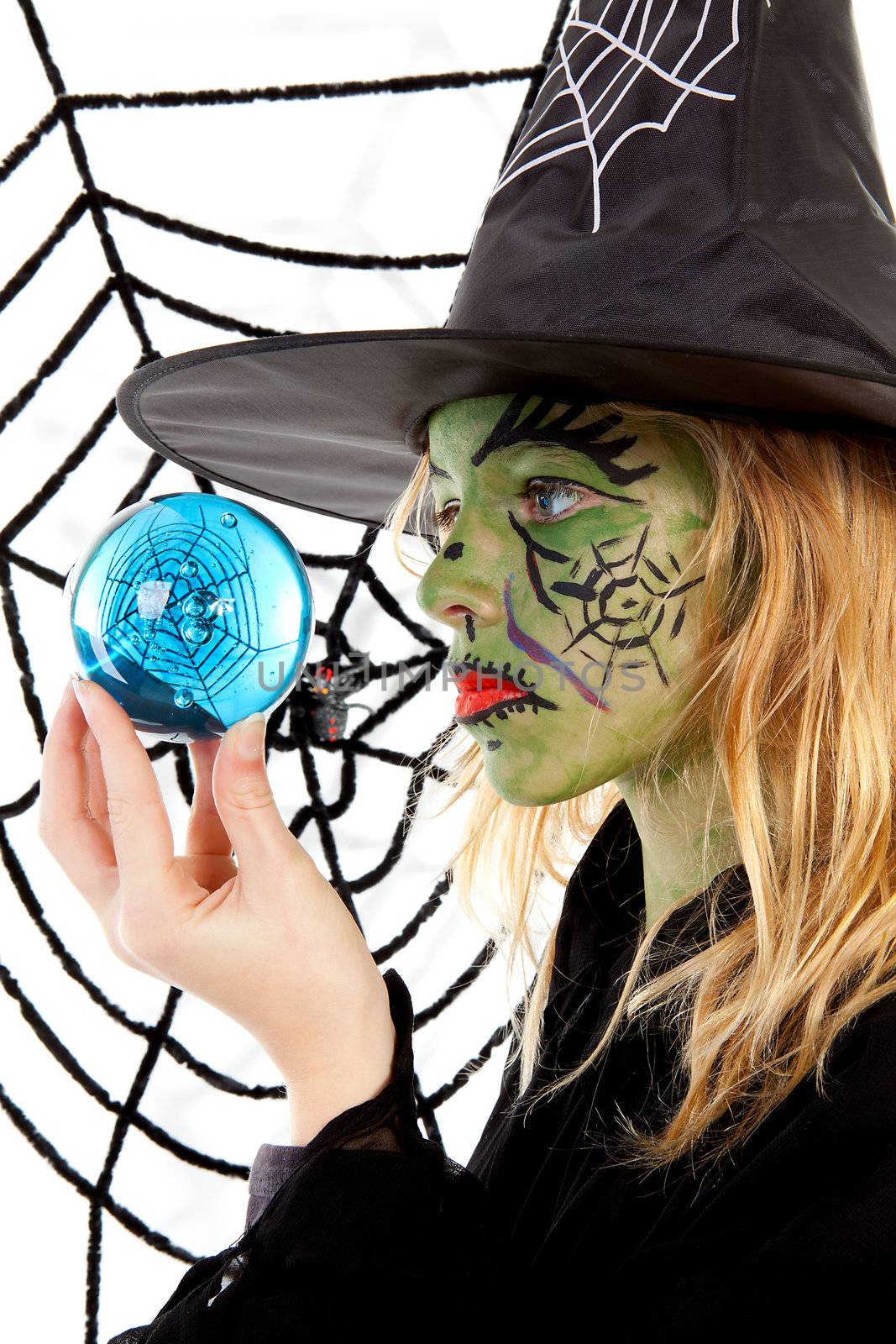 Portrait of green Halloween witch girl in closeup holding big blue marble