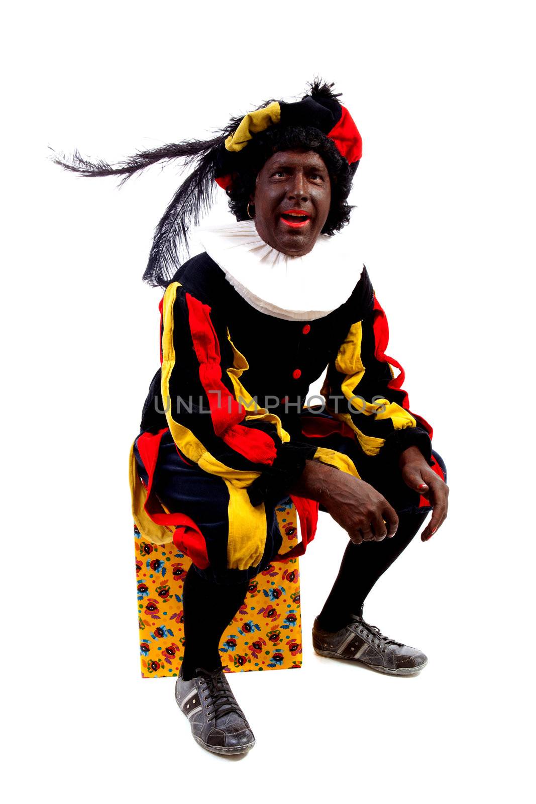 Zwarte piet ( black pete) typical Dutch character part of a traditional event celebrating the birthday of Sinterklaas in december over white background sitting on present