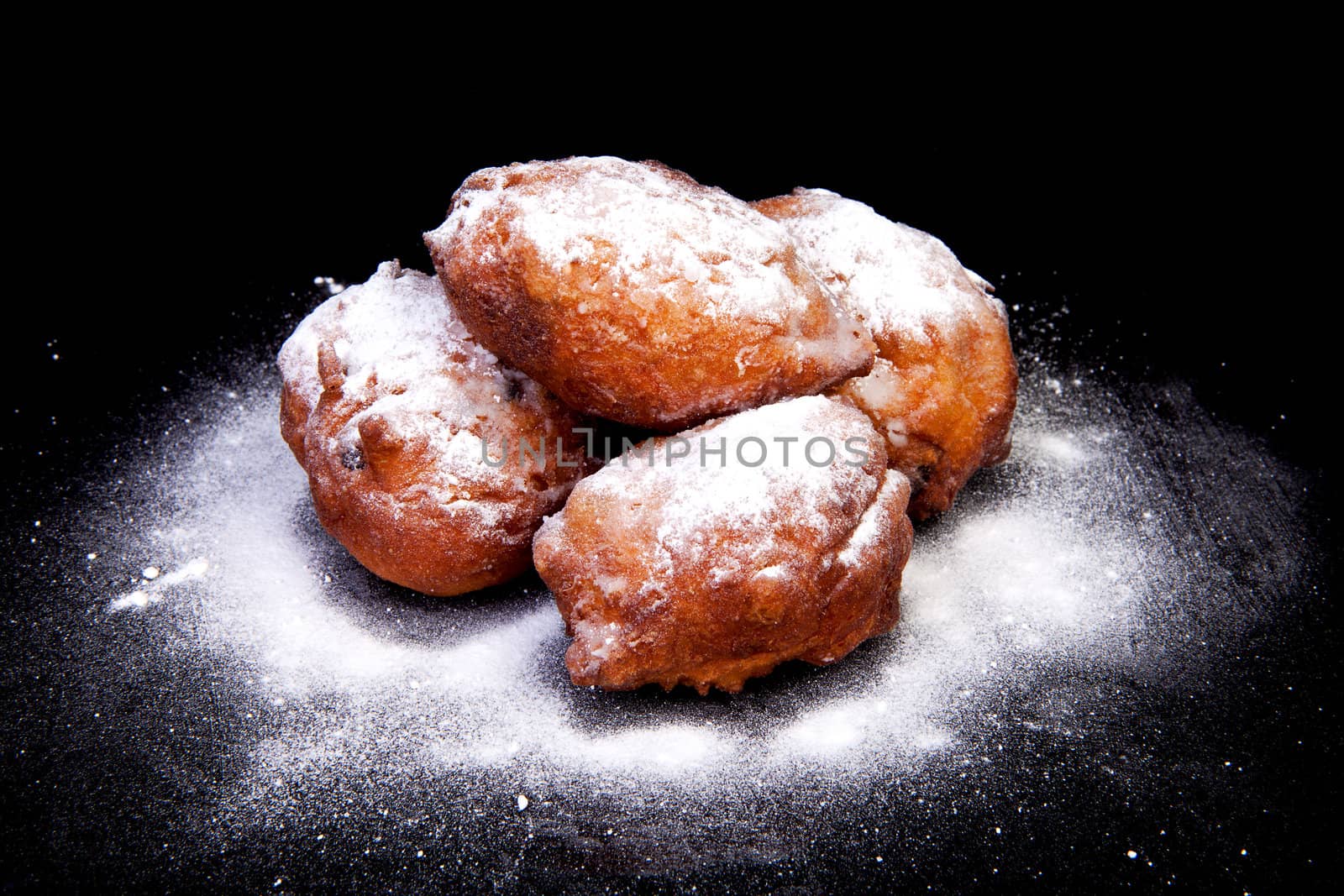 pile of Dutch donut also known as oliebollen with powdered sugar, traditional New Year's eve food isolated on black background 
