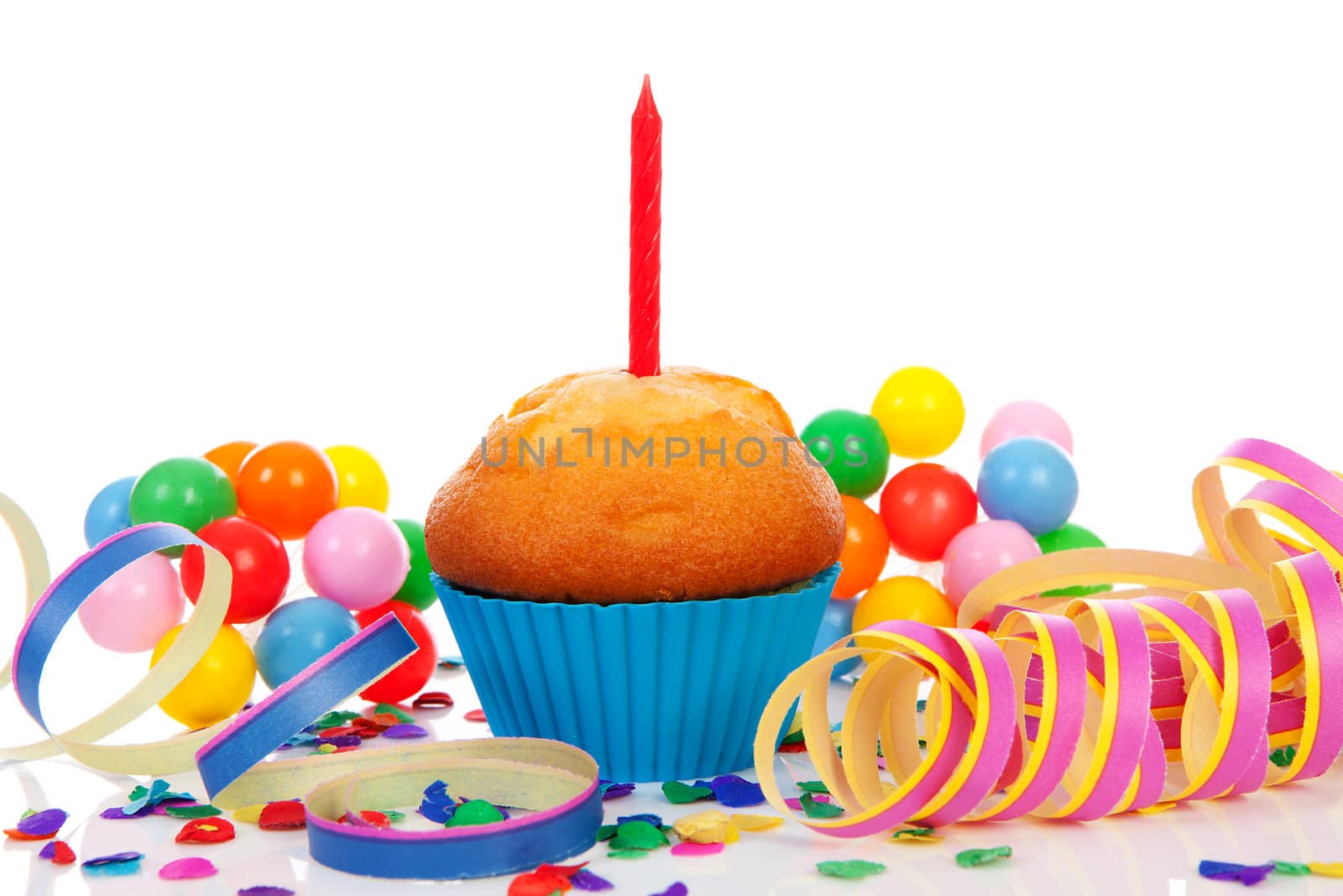 Birthday cupcake with candle, party streamers and colorful confetti over white background
