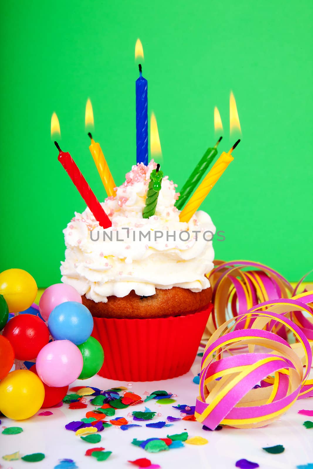 Birthday cupcake with lots of candles, party streamers and colorful confetti over green background