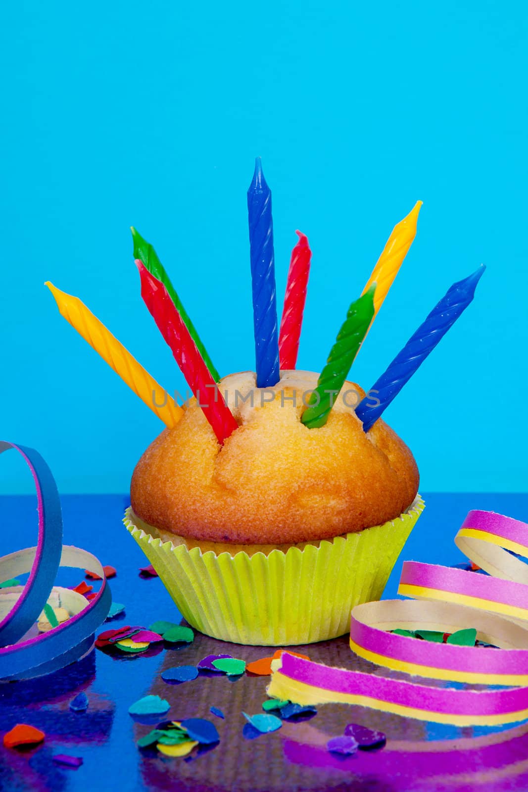 Birthday cupcake with lots of candles, party streamers and colorful confetti over blue background
