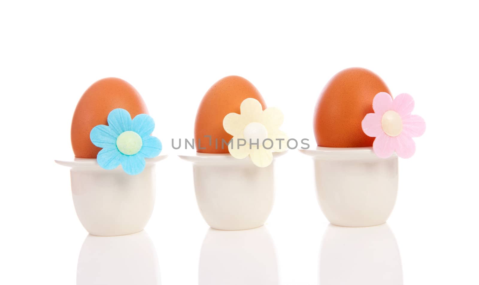 Three chicken eggs in holder with flowers over white background