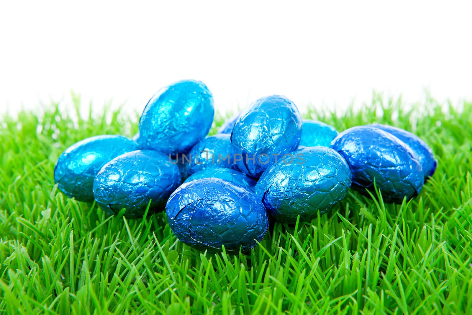 Blue chocolate easter eggs on grass over white background