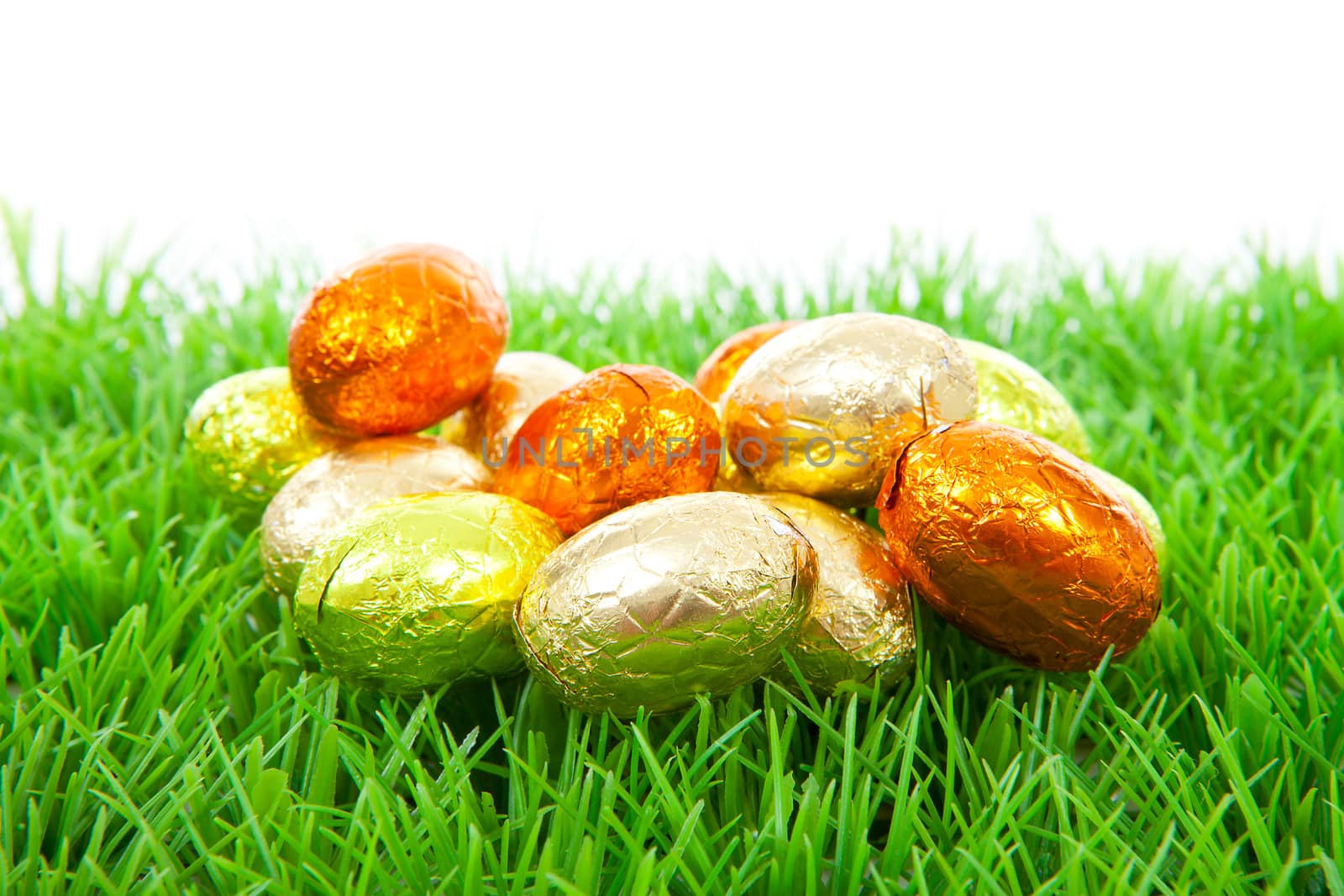 Golden chocolate easter eggs on grass over white background