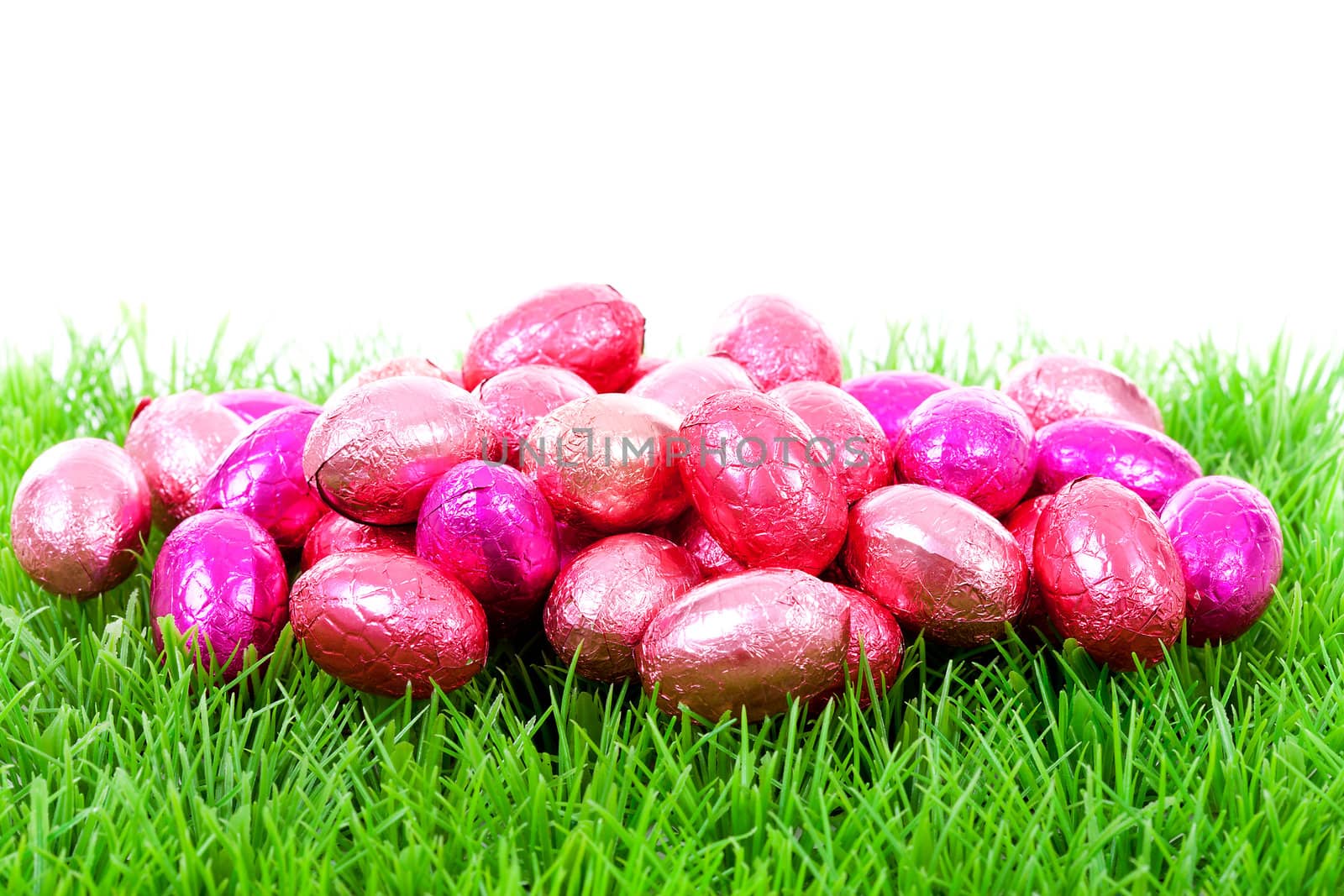 Pink chocolate easter eggs on grass over white background