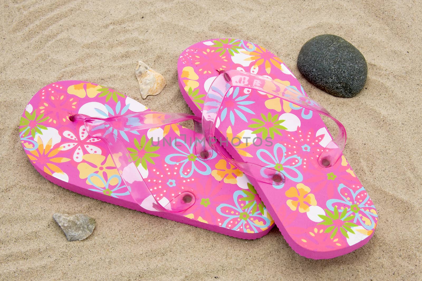 pink colored summer slippers lying on sand