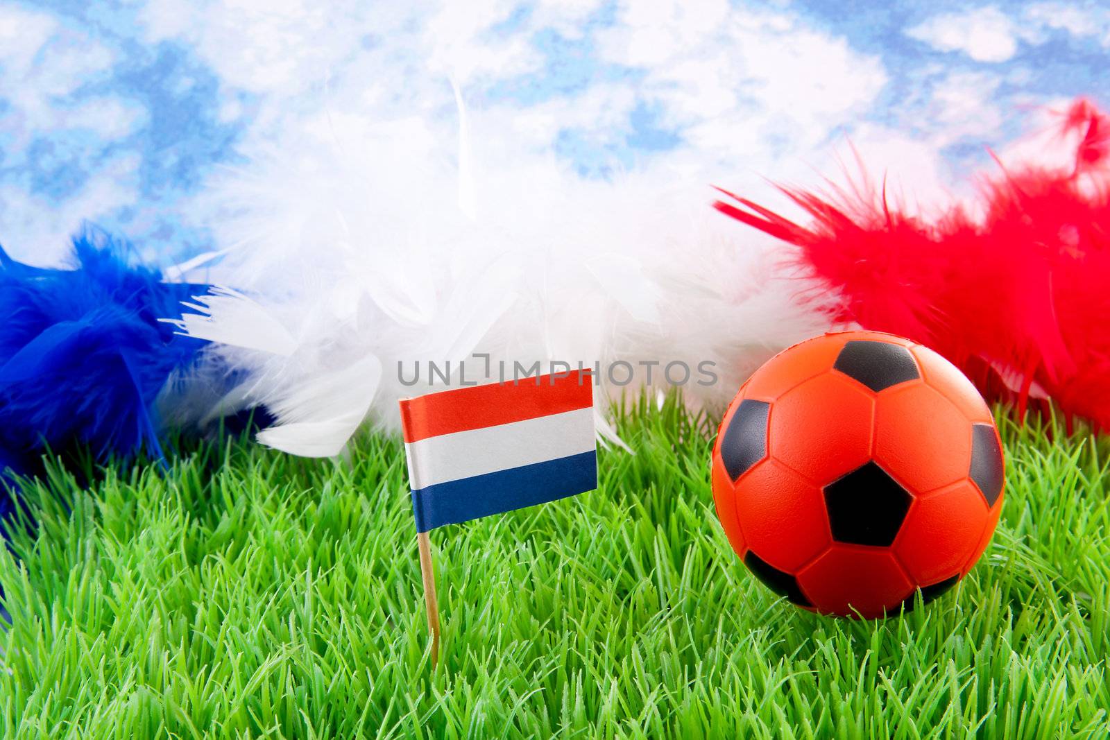 orange Soccer ball and Dutch flag on grass against blue cloudy sky