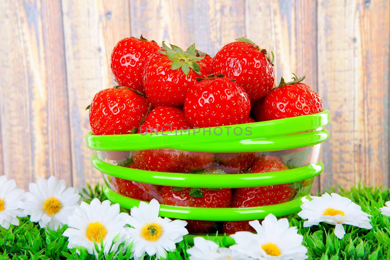 Bowl with fresh strawberries on grass over wooden background
