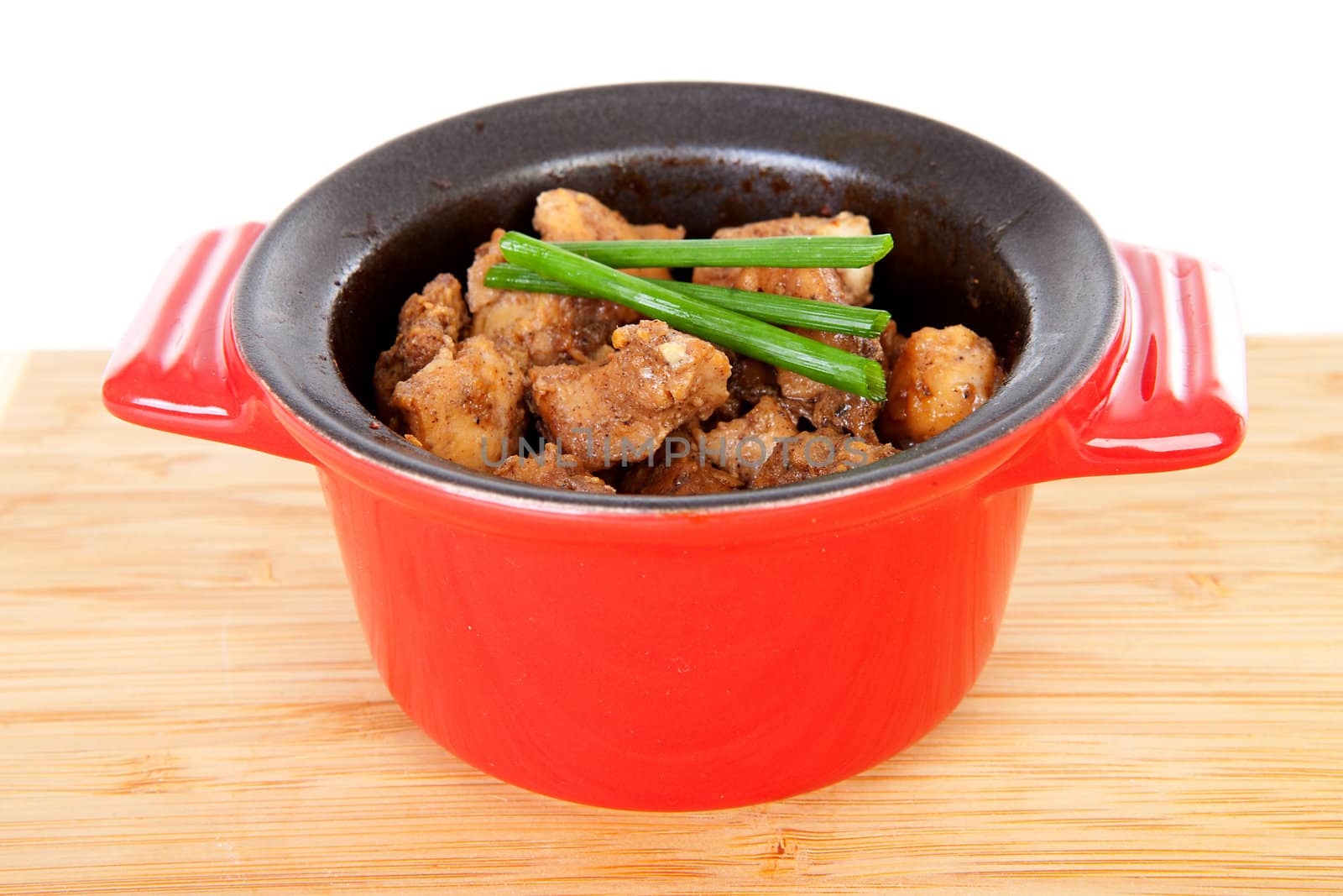 Baked chicken cubes in pan on wooden board over white background